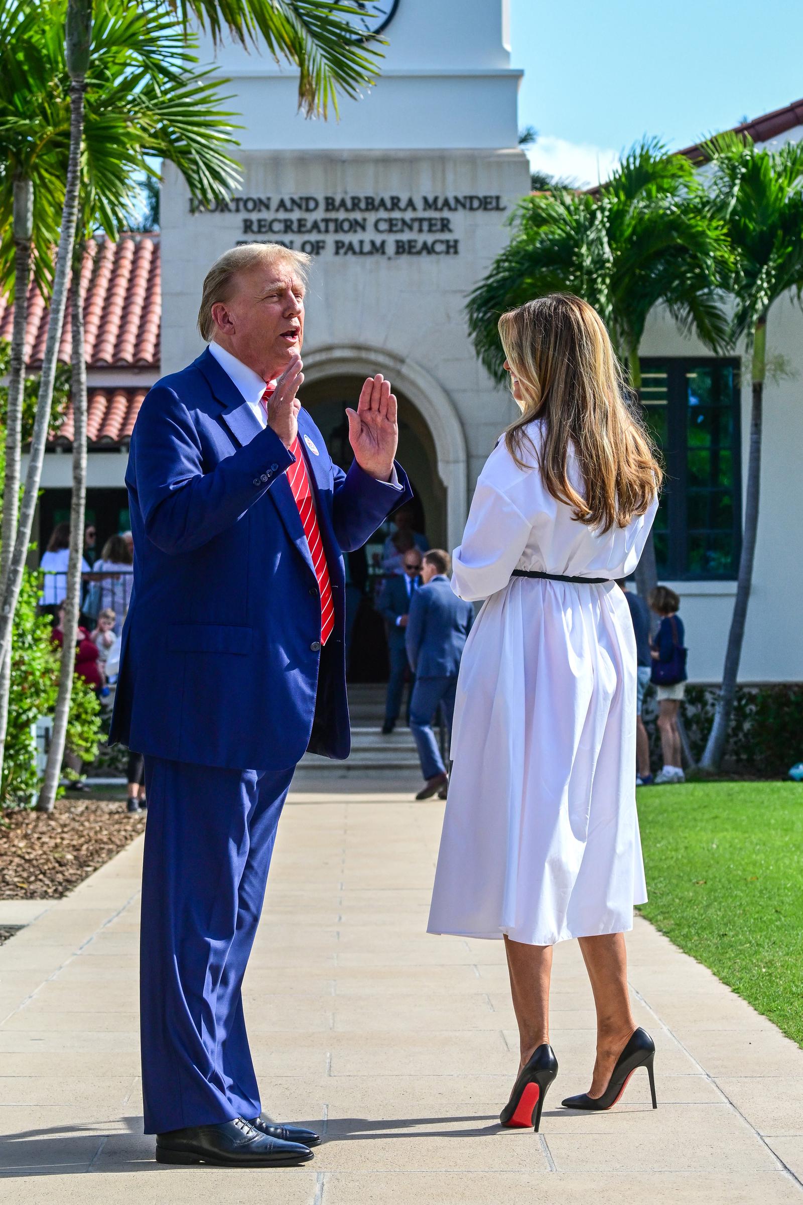 Die ehemalige First Lady Melania Trump unterhält sich mit Donald Trump, als sie am 19. März 2024 im Morton and Barbara Mandel Recreation Center in Palm Beach, Florida, am 19. März 2024. Sie trägt ein knackig weißes Midikleid mit Kragen, das an der Taille mit einem schmalen schwarzen Gürtel gerafft ist, sowie schwarze Lackpumps von Christian Louboutin mit spitzer Zehenpartie, himmelhohen Stiletto-Absätzen und leuchtend roten Lacksohlen.
