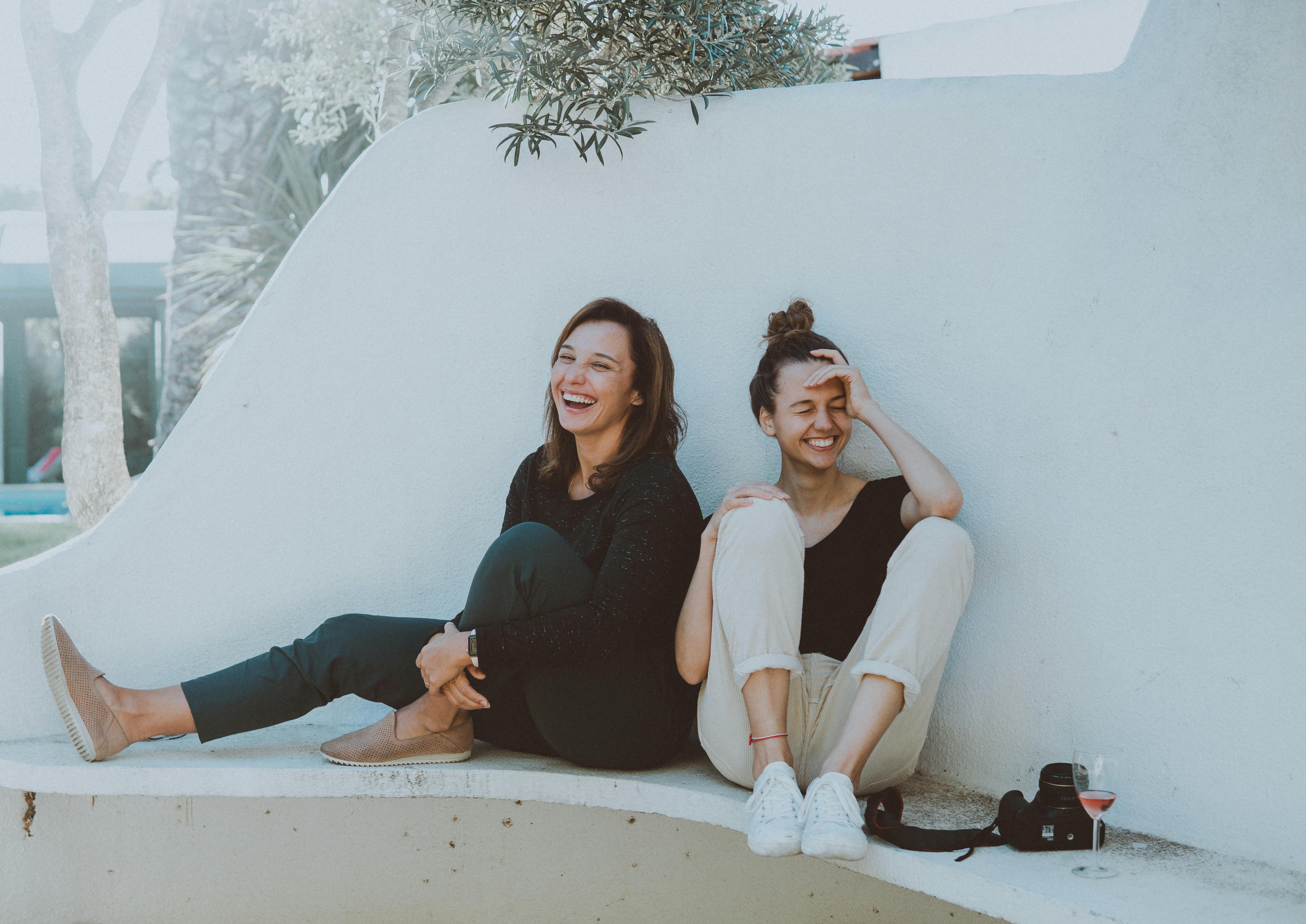 Zwei beste Freundinnen sitzen Rücken an Rücken und lachen | Quelle: Elle Hughes auf Pexels