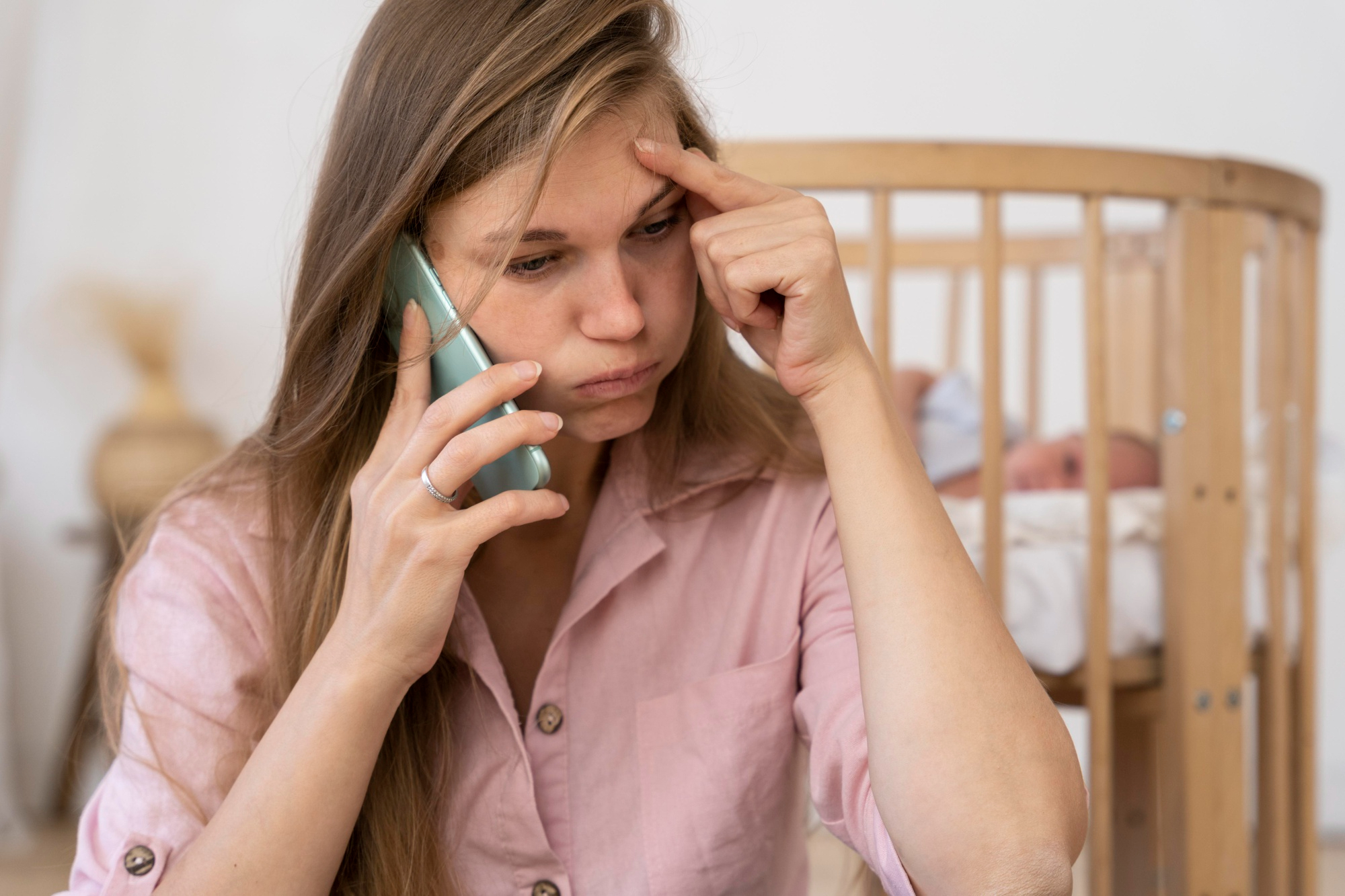 Eine frustrierte Frau telefoniert mit ihrem Baby, das in einem Kinderbett hinter ihr liegt | Quelle: Freepik