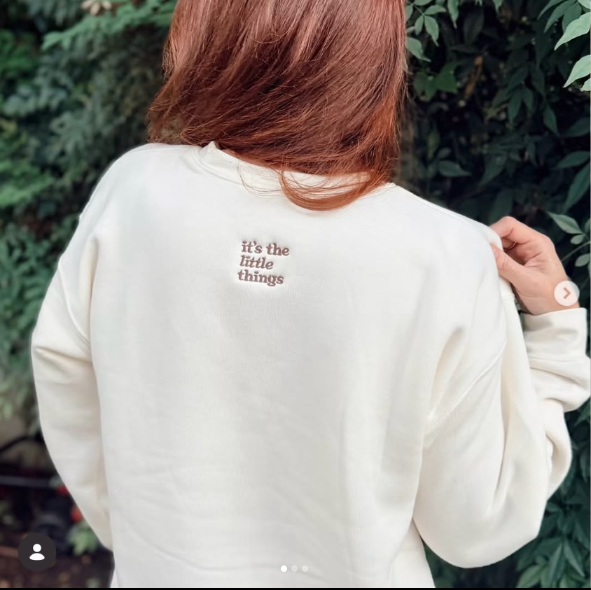 Auf dem cremefarbenen Sweatshirt ist oben auf dem Rücken in brauner Stickerei „It’s the Little Things“ zu lesen. | Quelle: Instagram/momsofferingmore
