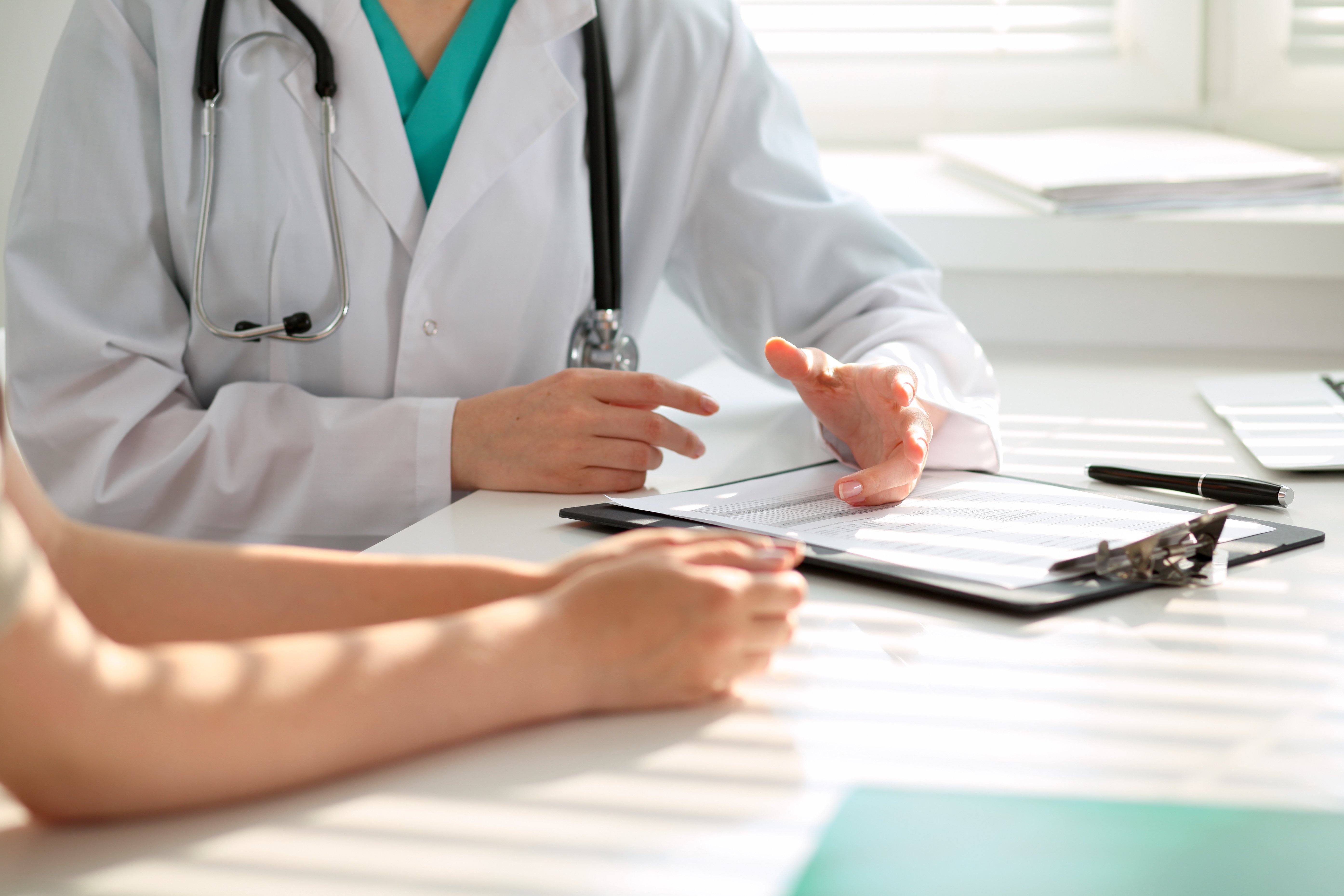 Arzt und Patient diskutieren etwas, nur Hände am Tisch | Quelle: Shutterstock