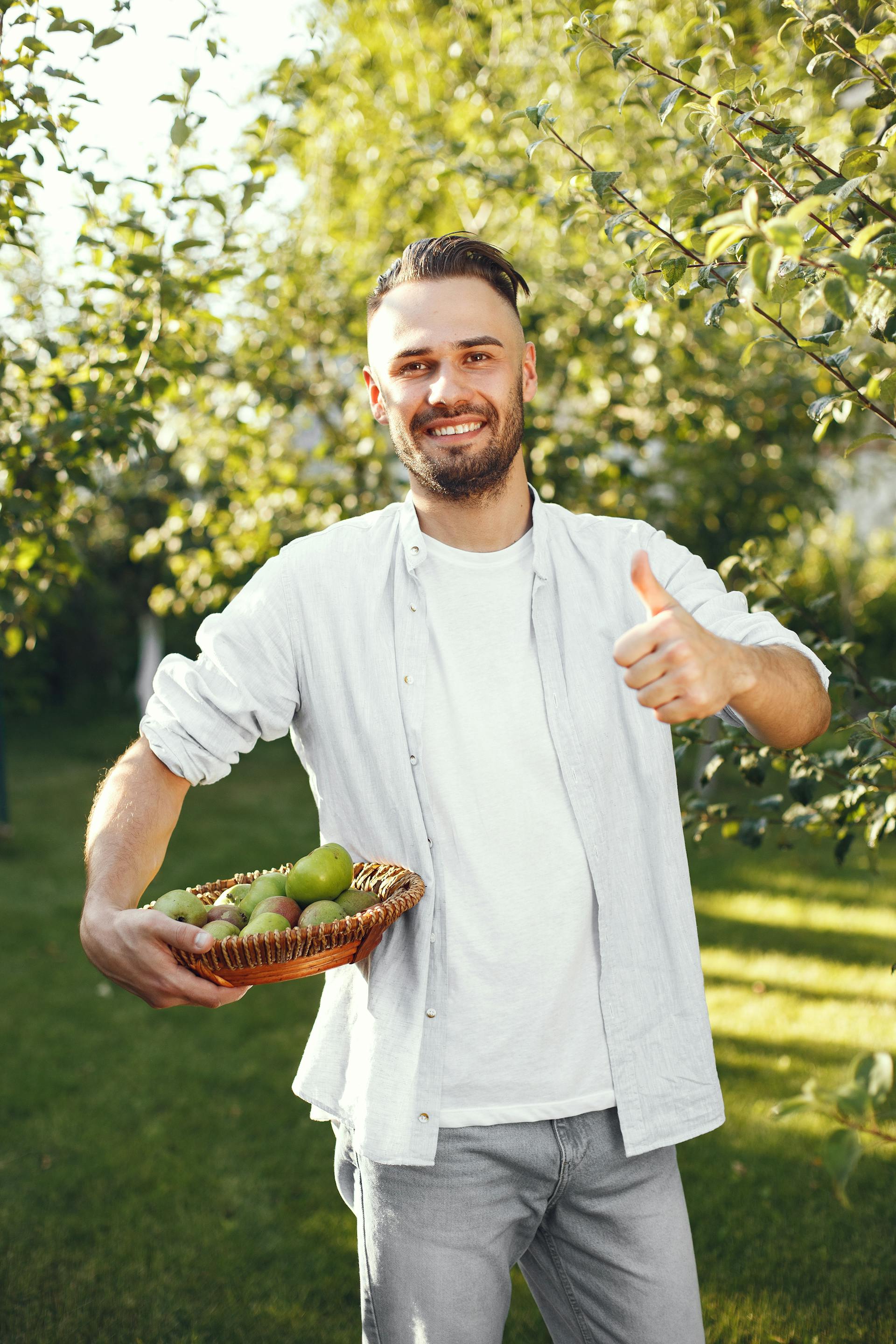 Ein Mann steht in seinem Garten und hält einen Korb mit Früchten | Quelle: Pexels