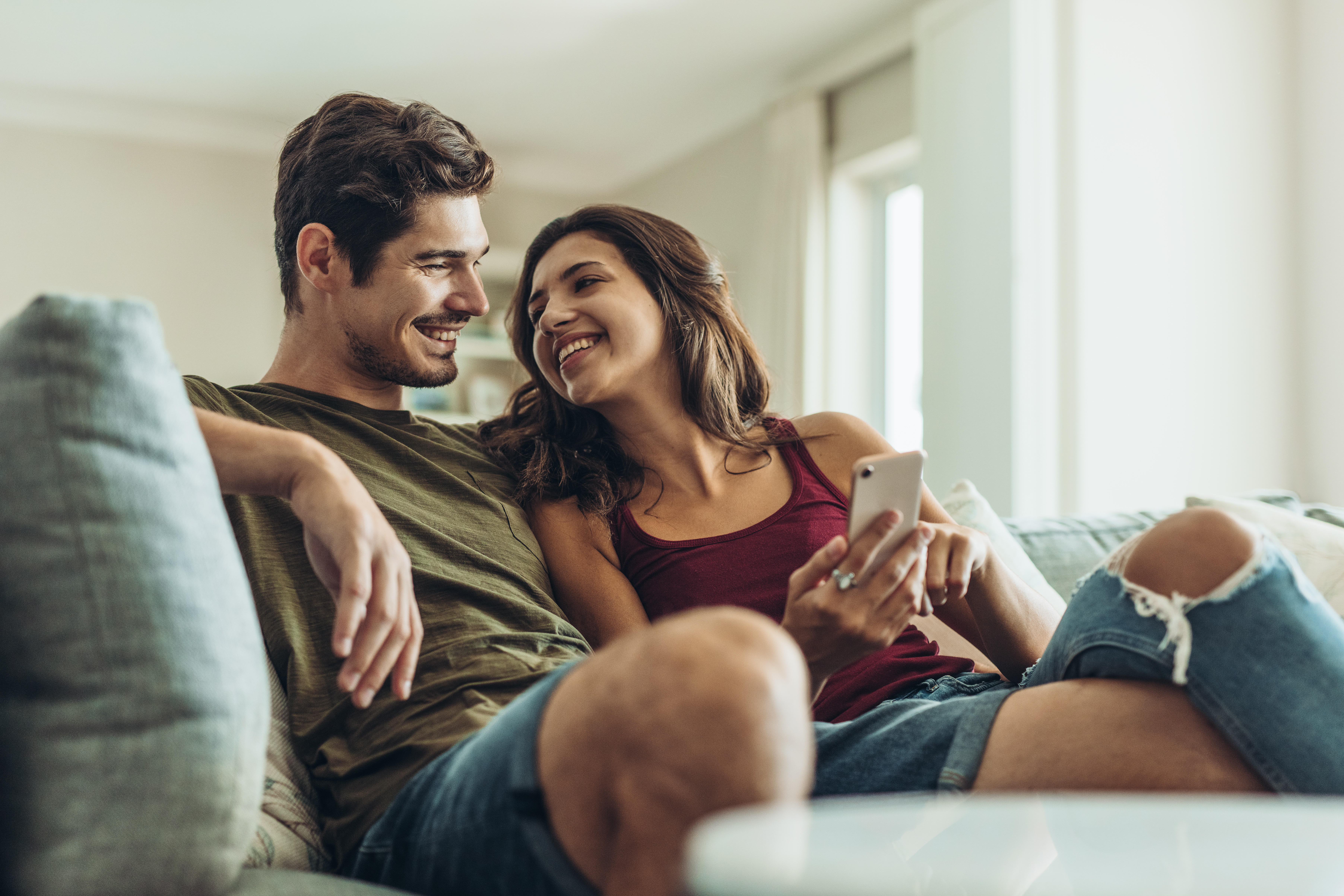 Ein junges Paar sitzt lachend auf einem Sofa und schaut auf ein Telefon | Quelle: Shutterstock