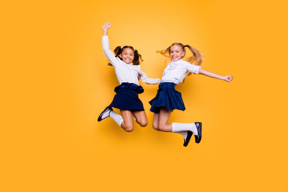 Zwei Mädchen hüpfen fröhlich in der Schuluniform. | Quelle: Shuttestock