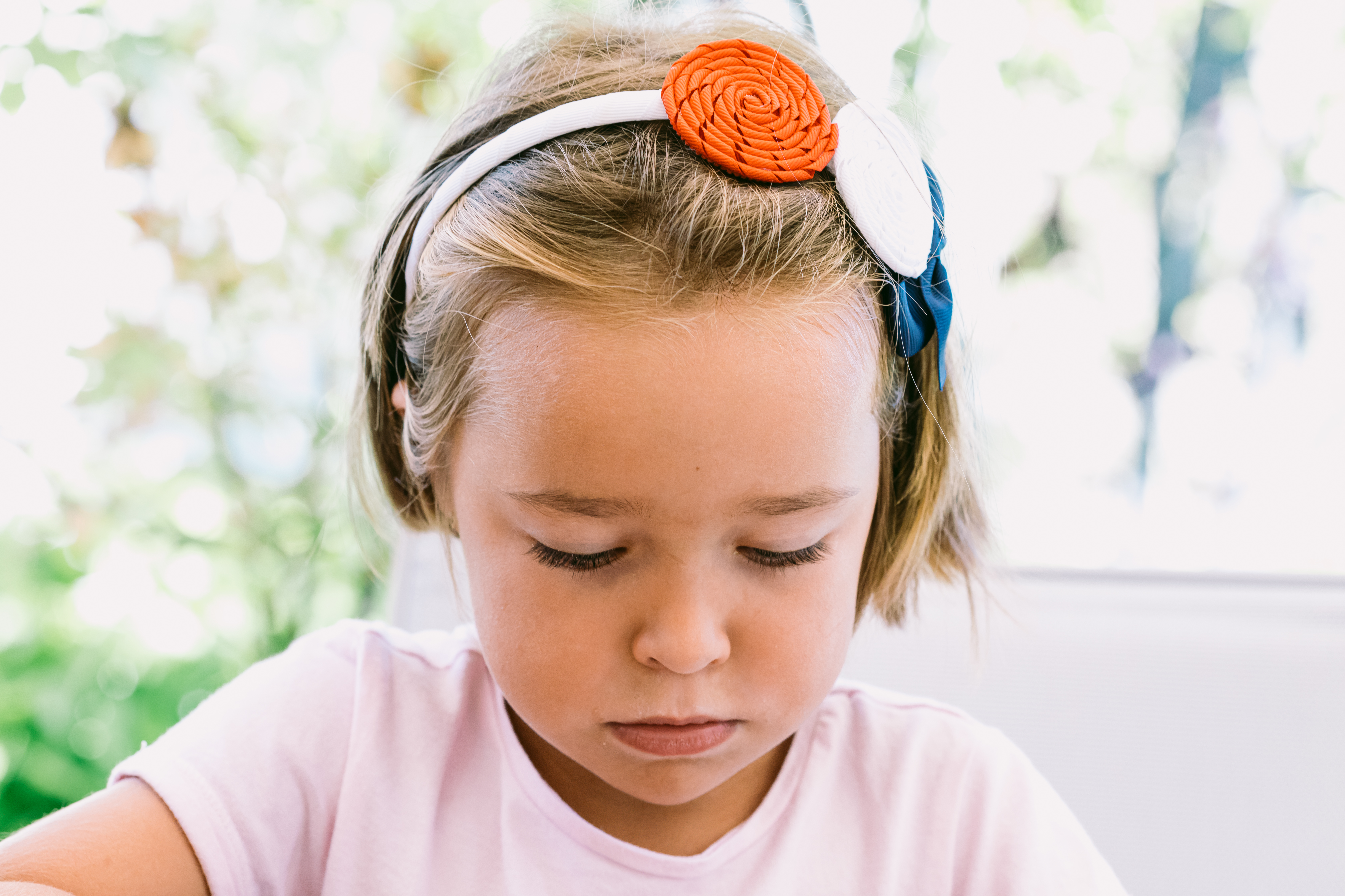 Porträt eines ernsten blondhaarigen kleinen Mädchens, das ein weißes Stirnband mit blauen, roten und weißen Verzierungen trägt, mit einem Garten im Hintergrund | Quelle: Getty Images