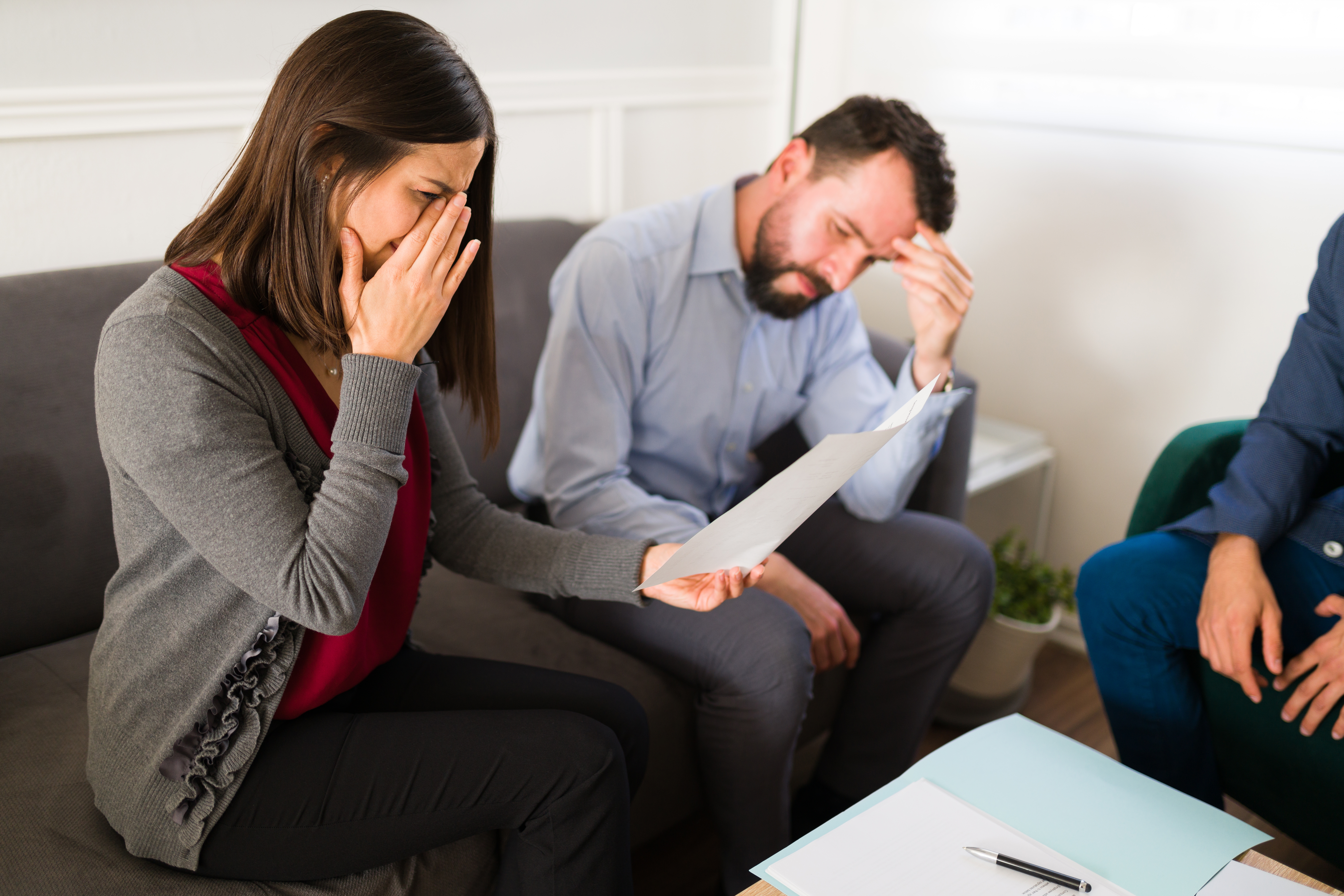 Eine weinende Frau mit einem Blatt Papier in der Hand und einem Mann, der neben ihr sitzt | Quelle: Shutterstock