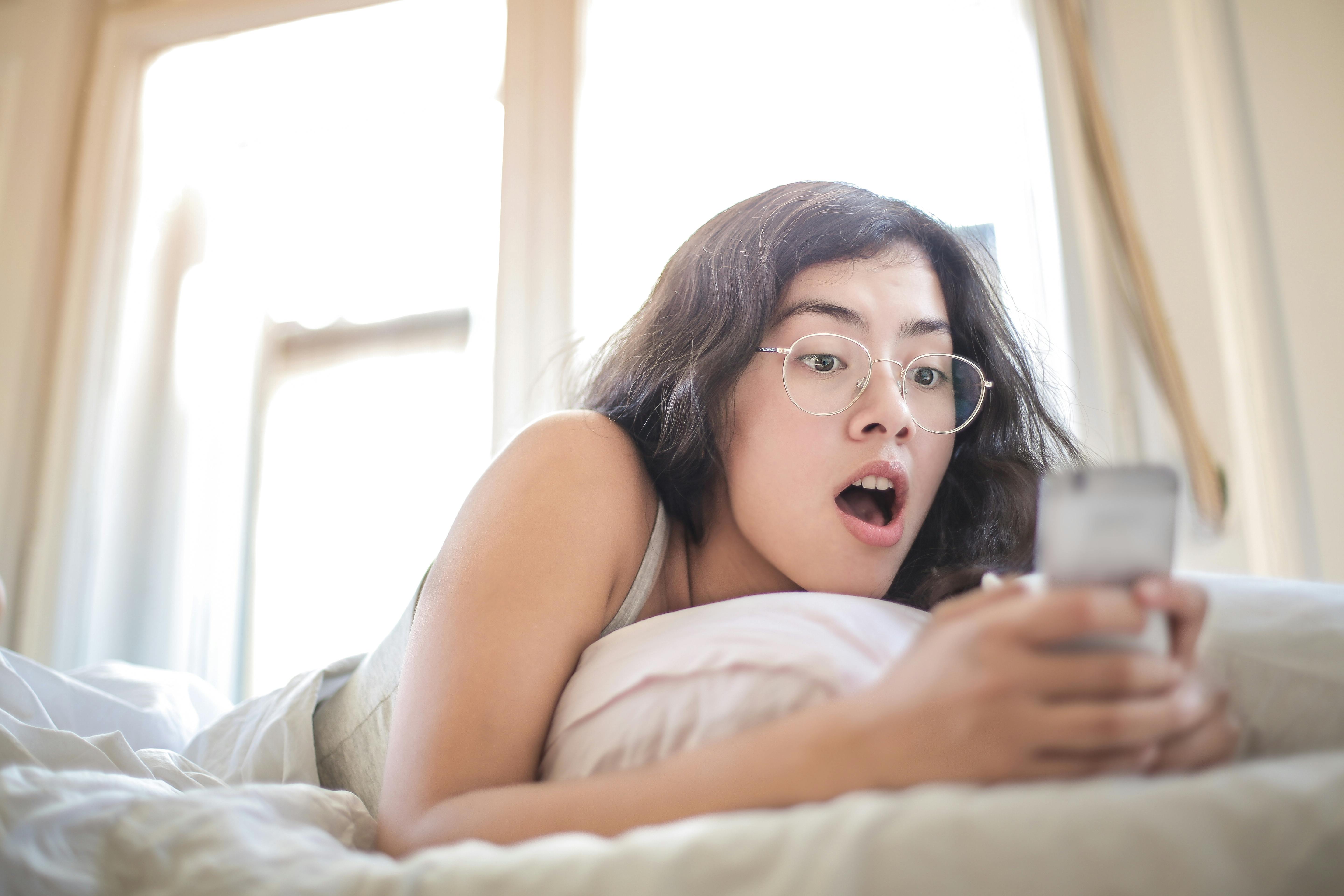 Eine geschockte Frau, die auf einem Bett liegt und ein Telefon hält und darauf schaut | Quelle: Pexels