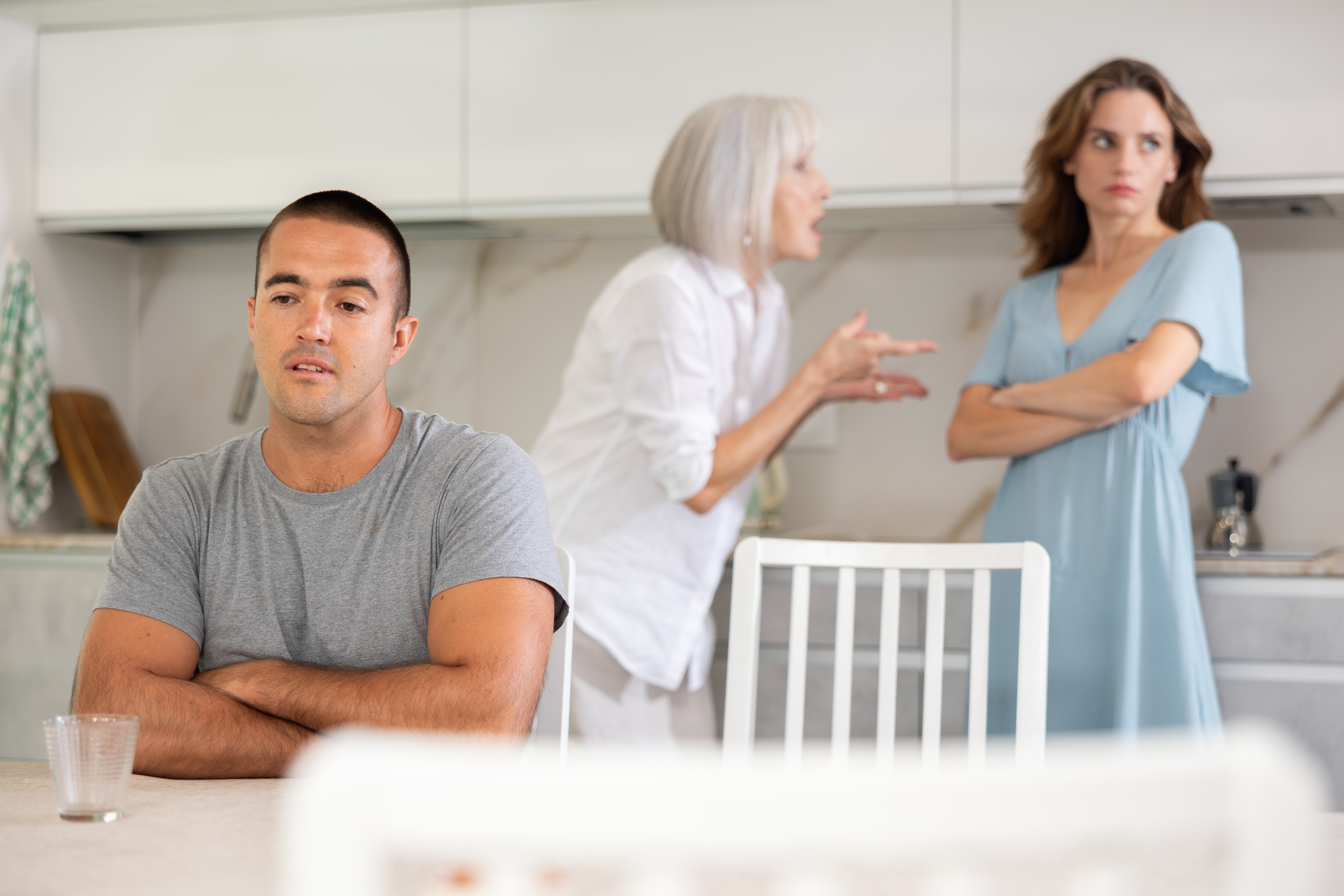 Eine ältere Frau streitet sich mit einer jüngeren Frau, die wegschaut, während ein anderer Mann vor ihnen sitzt | Quelle: Shutterstock