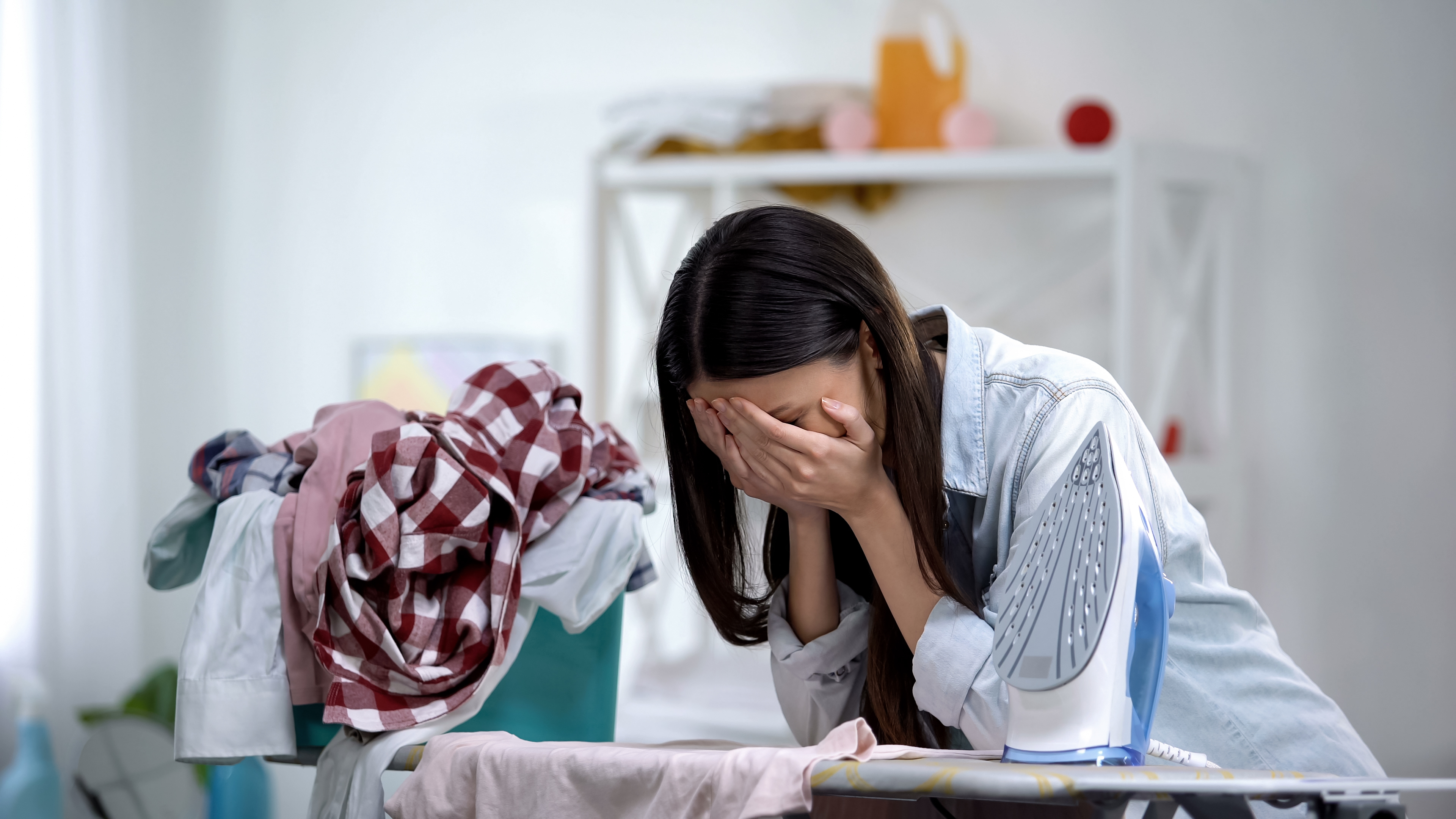 Eine Frau hat einen emotionalen Zusammenbruch, während sie sich auf das Bügelbrett stützt | Quelle: Shutterstock