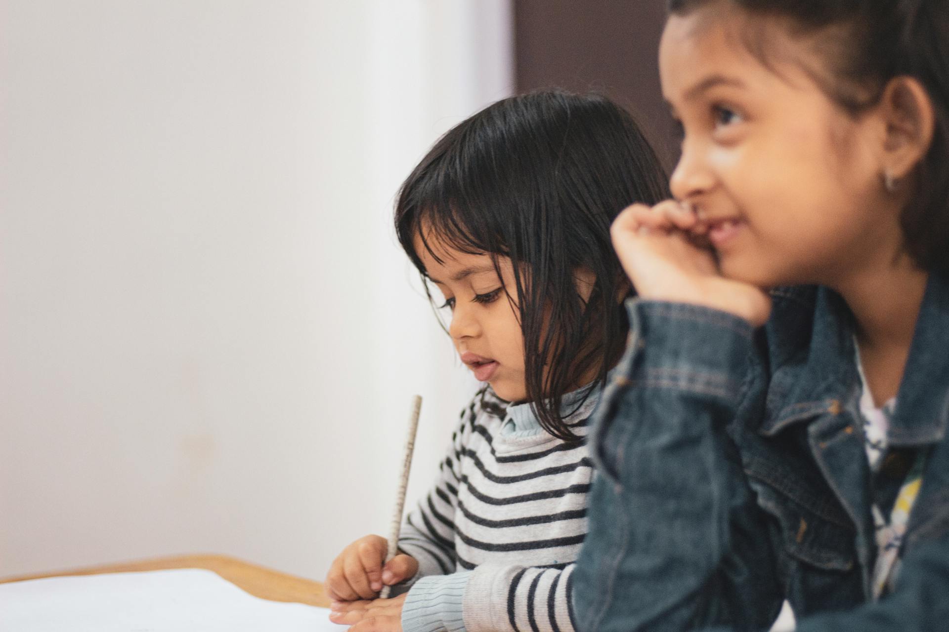 Mädchen sitzen an einem Schreibtisch, ein Mädchen schreibt auf Papier | Quelle: Pexels