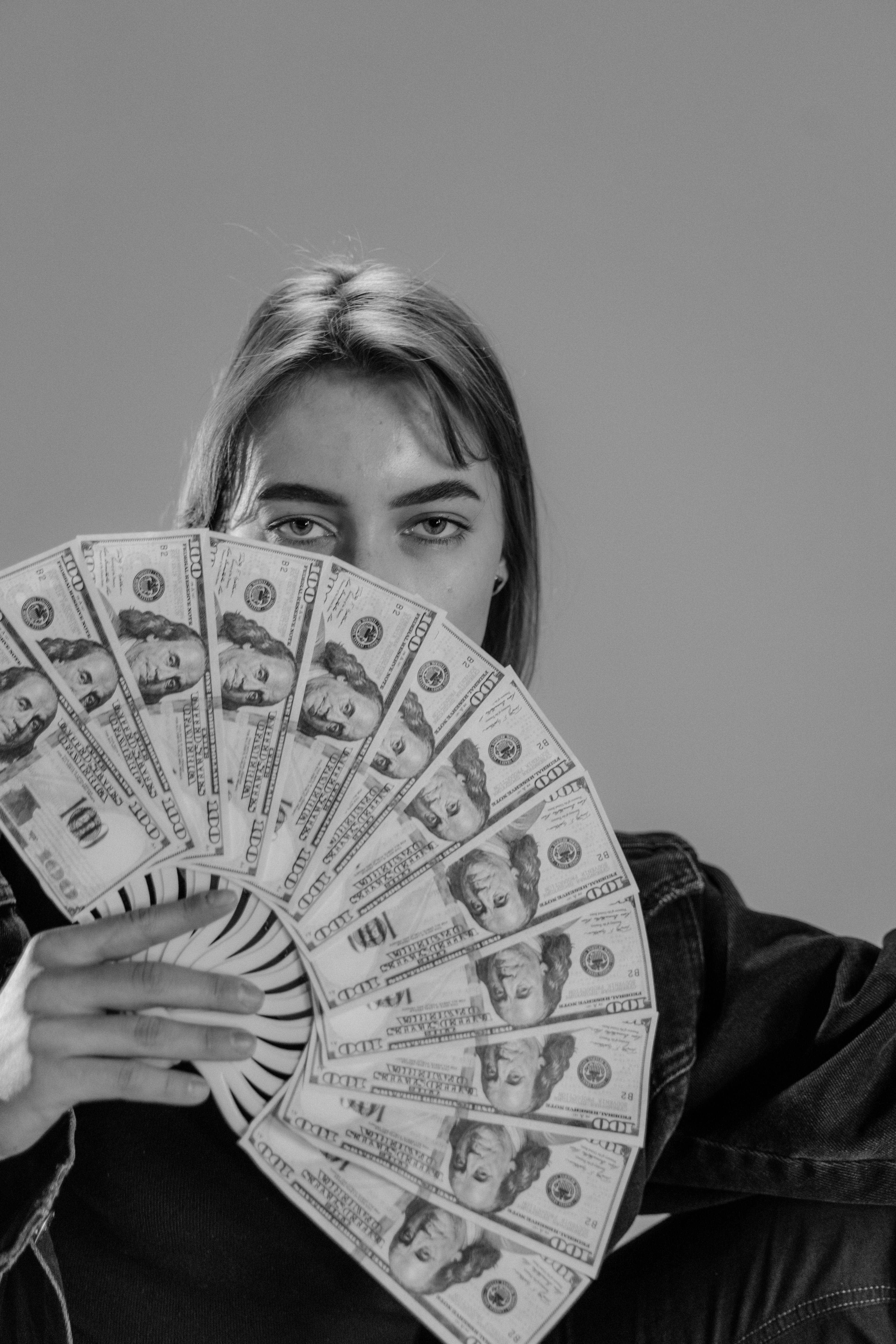 Eine Frau, die einen 100-Dollar-Schein wie einen Fächer hält, der einen Teil ihres Gesichts bedeckt | Quelle: Pexels