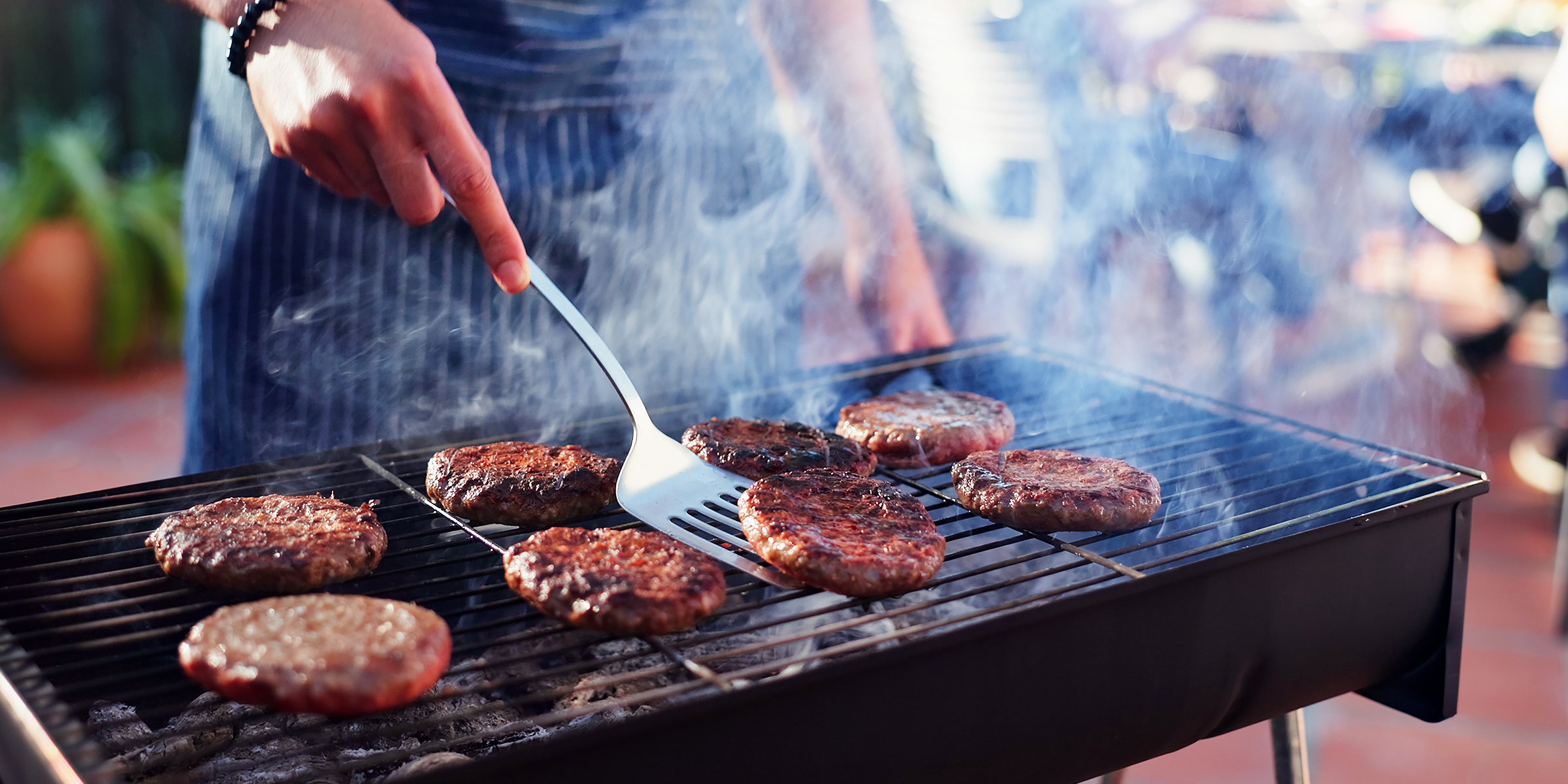 Eine Person grillt Burger auf einem rauchigen Hinterhofgrill | Quelle: Shutterstock