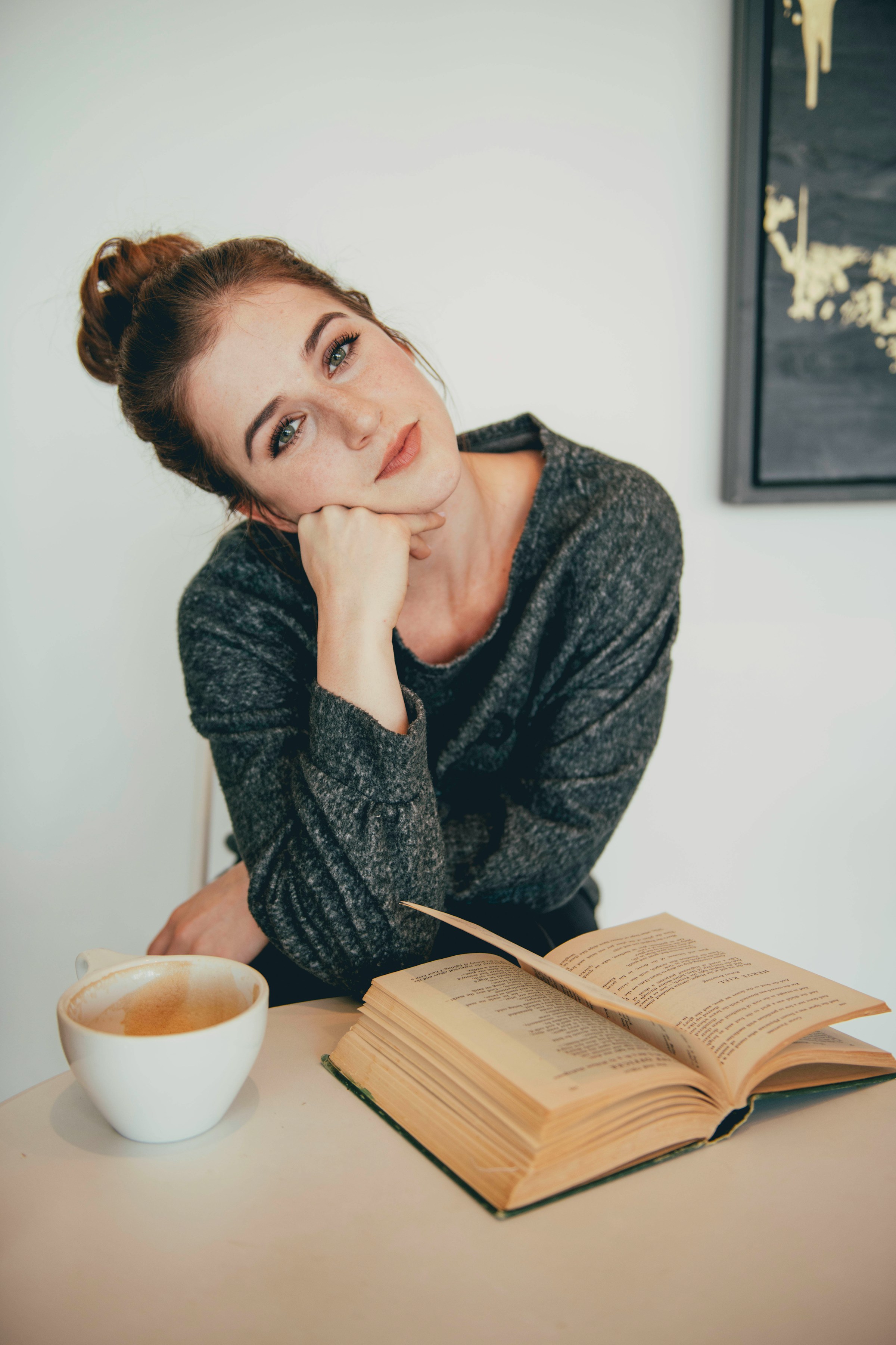 Eine Frau sitzt bei einer Tasse Kaffee und einem aufgeschlagenen Buch | Quelle: Unsplash