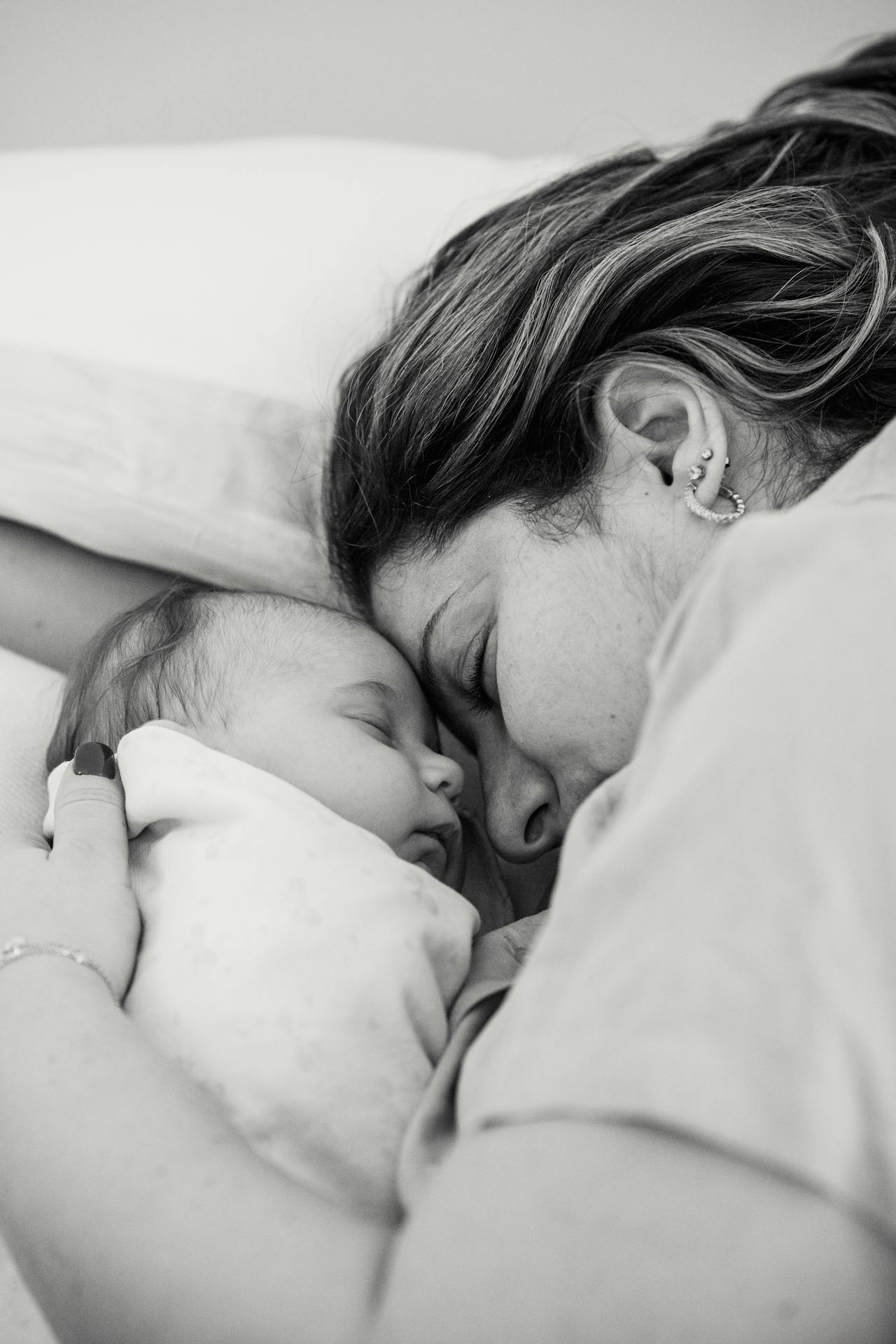 Graustufenaufnahme einer Frau, die neben ihrem Baby liegt | Quelle: Pexels