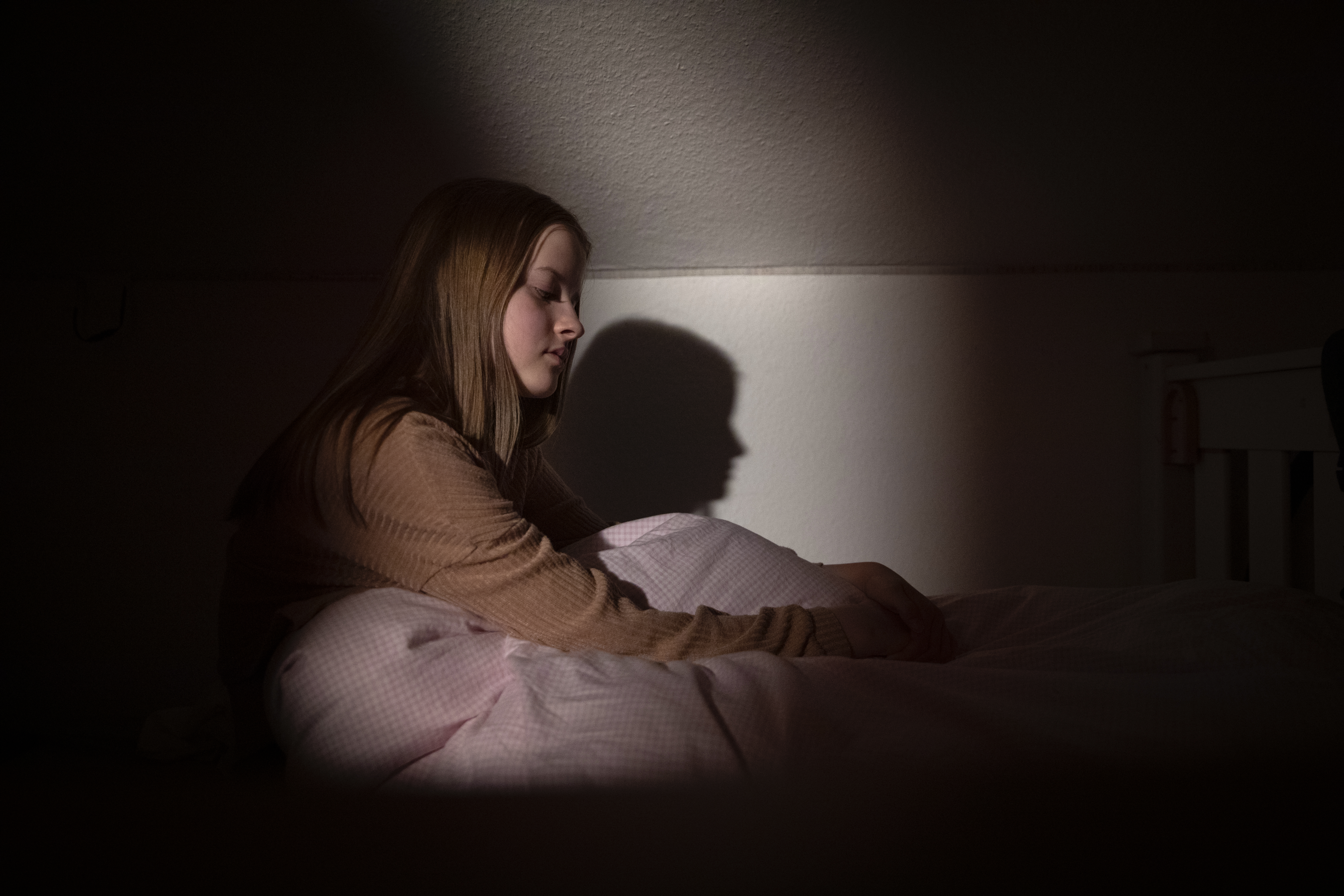 Jugendliche, die nachts bei schwachem Licht im Bett sitzt, mit einem Gesichtsausdruck, der Verzweiflung und Traurigkeit ausdrückt | Quelle: Getty Images