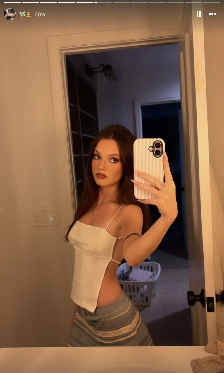 Harper Lockwood macht ein Selfie vor dem Badezimmerspiegel – sie trägt ein weißes, rückenfreies Neckholder-Crop-Top und dazu einen gestreiften Rock, was ihr langes dunkles Haar und ihr auffälliges Augen-Make-up besonders gut zur Geltung bringt. | Quelle: Instagram/harper.lockwoodd