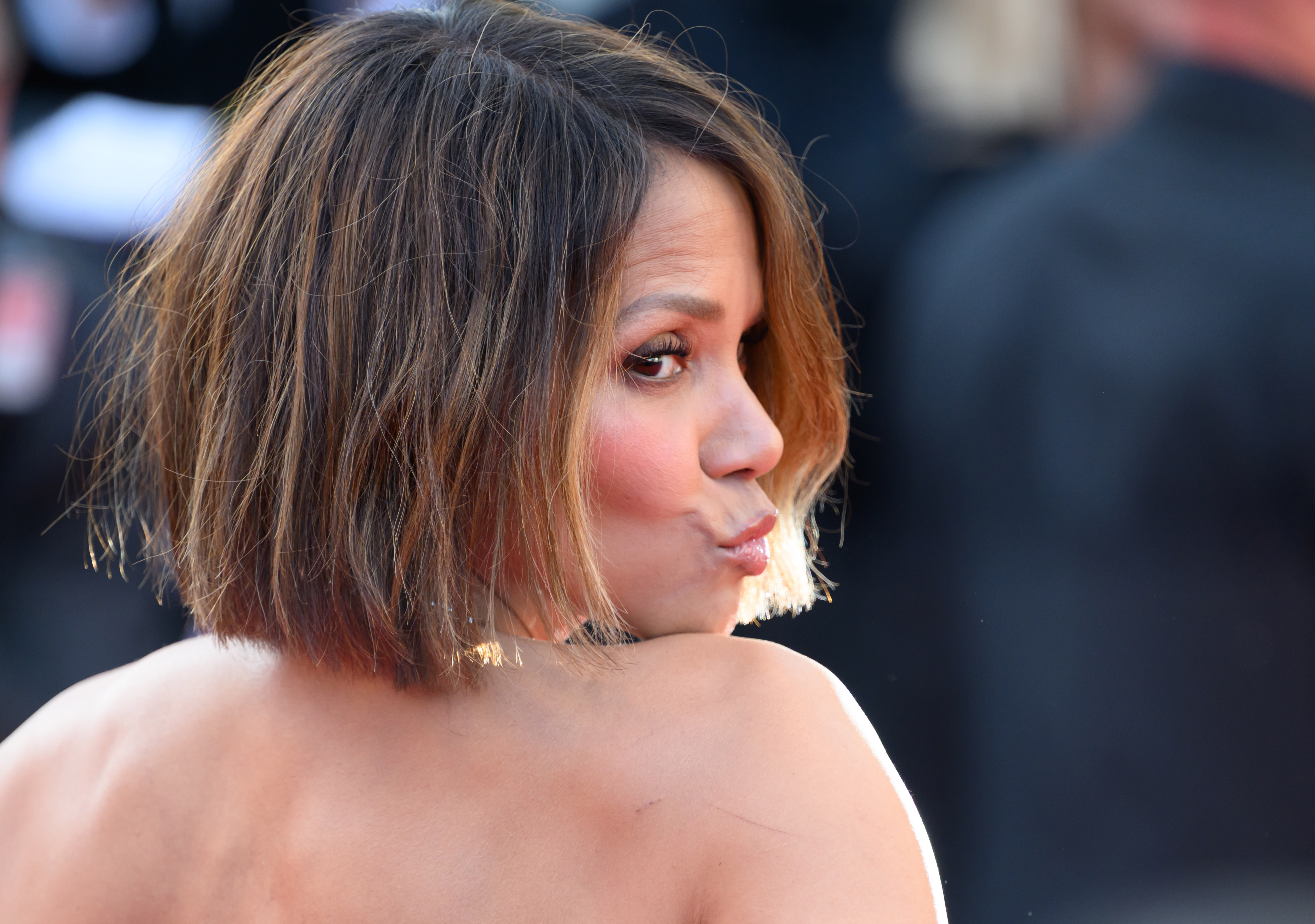 Halle Berry schürzt ihre Lippen in einer verspielten Pose und blickt mit einem frechen Blick über ihre Schulter zurück, während sie auf dem roten Teppich in die Kameras schaut.