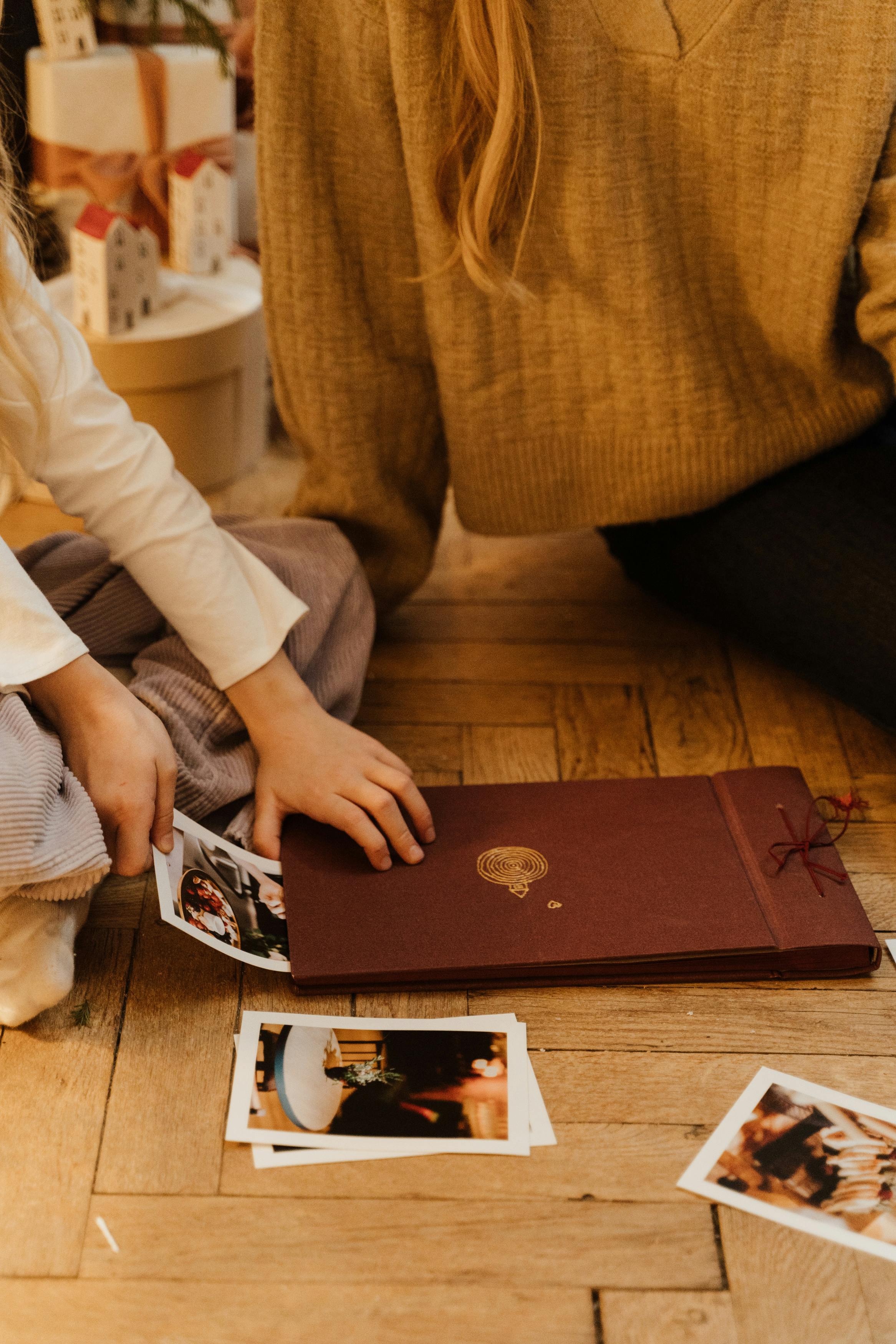 Ein Kind nimmt Fotos aus einem Buch heraus, während ein Erwachsener neben ihm sitzt | Quelle: Pexels