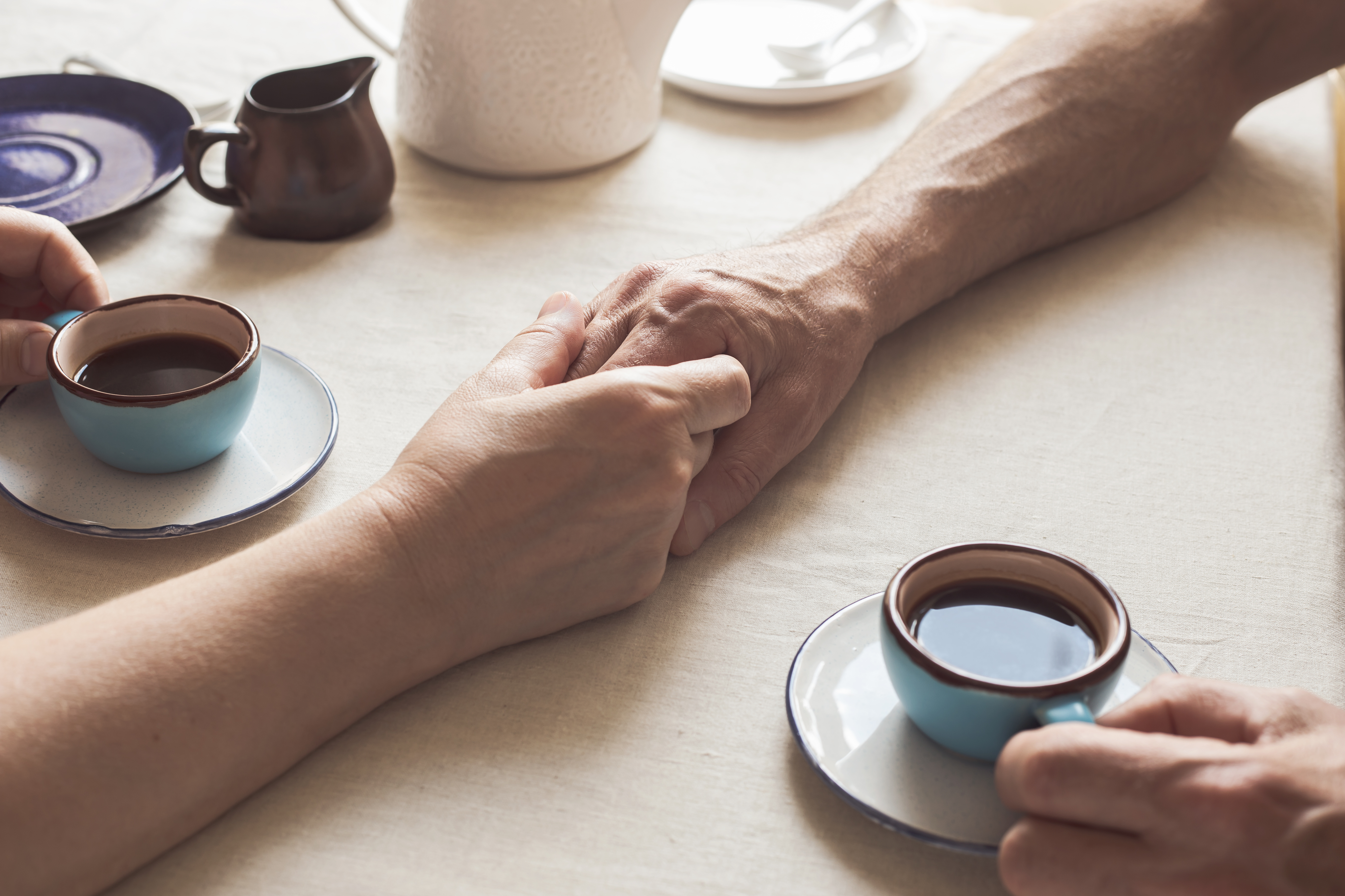 Ausgeschnittenes Bild eines älteren Paares, das sich an den Händen hält und Kaffee trinkt | Quelle: Getty Images