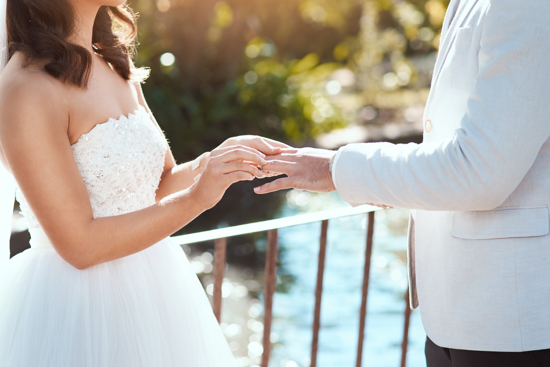 Die Braut zieht einen Ring an den Finger ihres Bräutigams, während sie an ihrem Hochzeitstag im Freien steht | Quelle: Getty Images