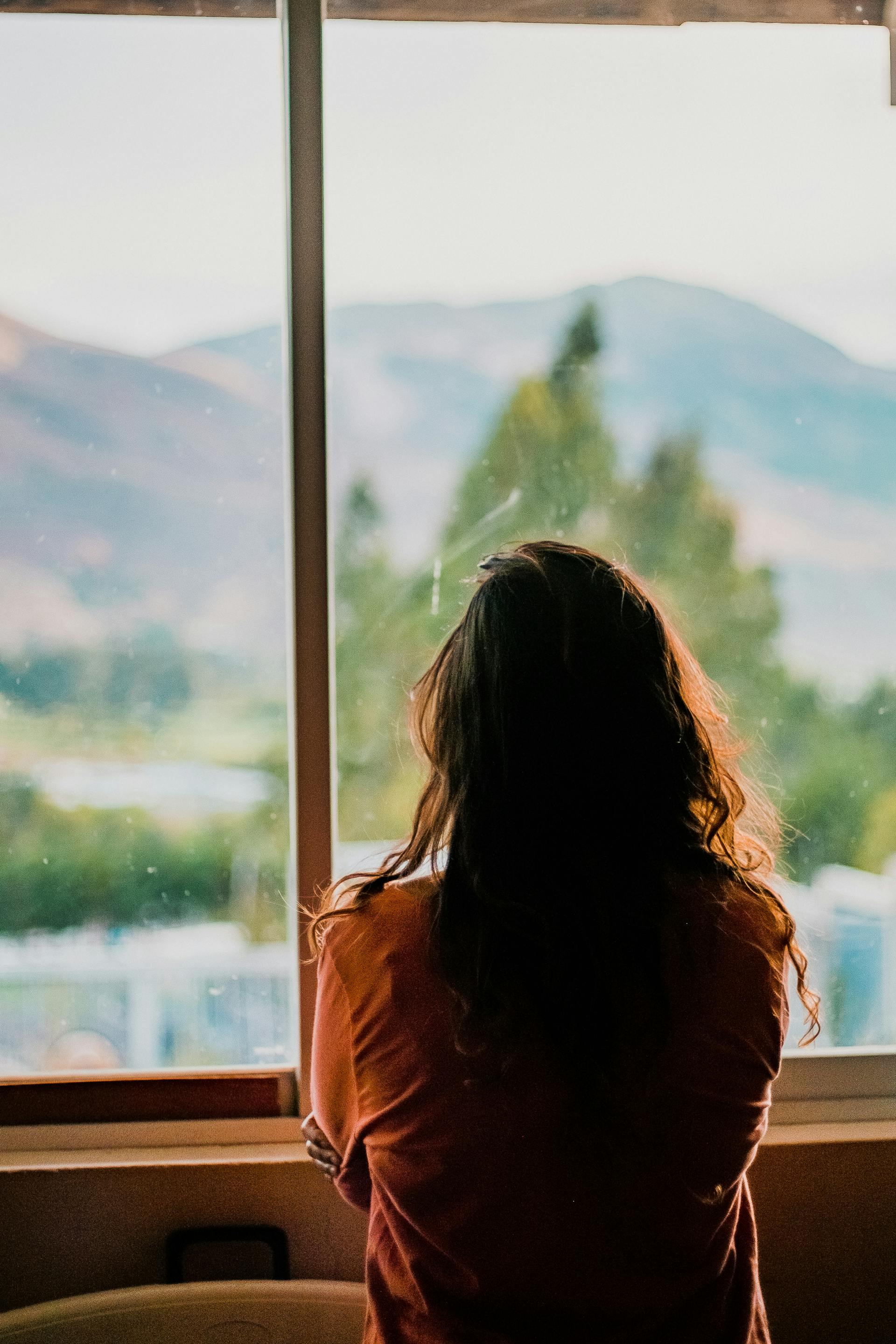 Rückansicht einer Frau, die mit verschränkten Armen aus dem Fenster schaut | Quelle: Pexels