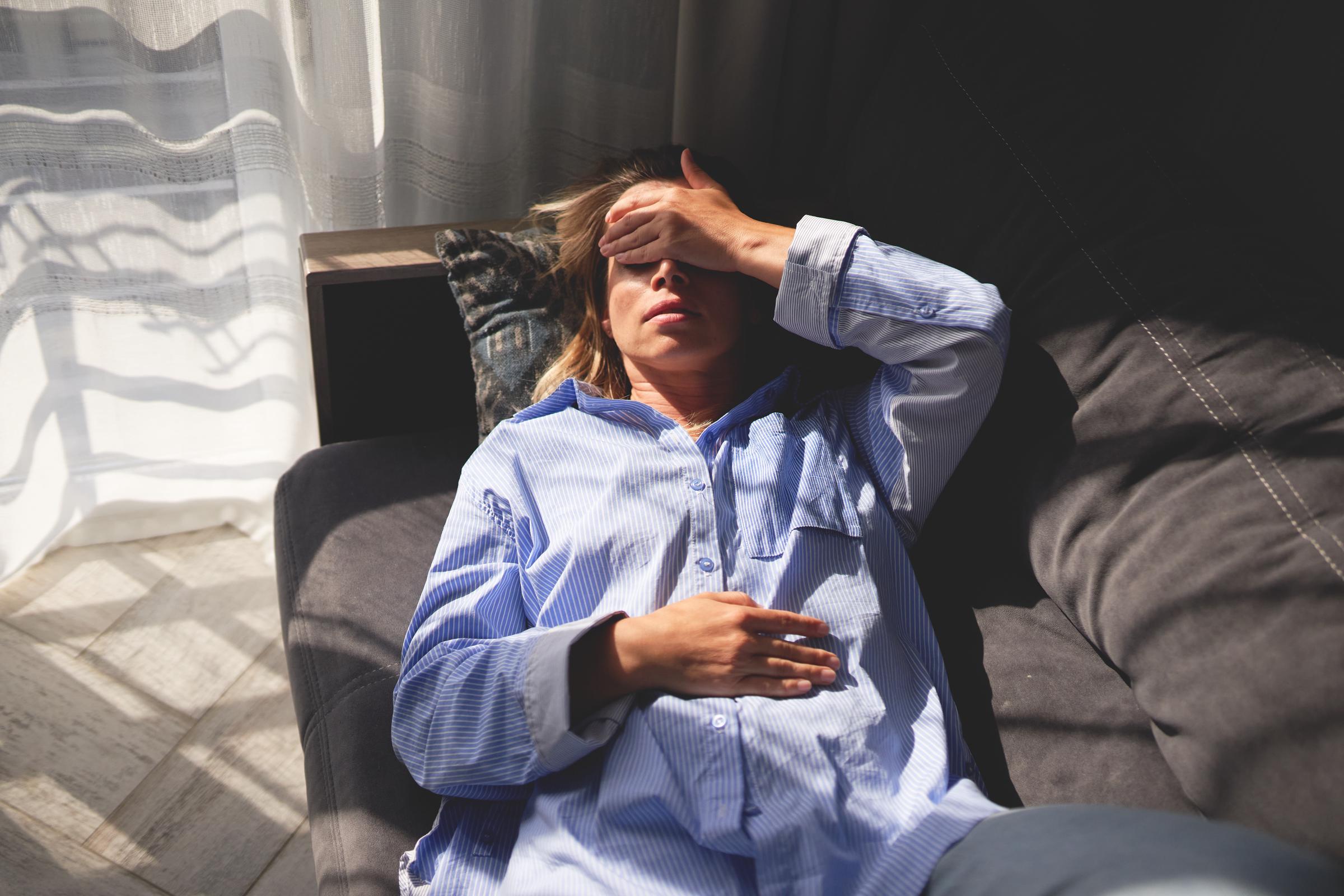 Frau, die auf einer Couch liegt, die Hand auf der Stirn und die Augen geschlossen, was auf Erschöpfung oder Stress hindeutet | Quelle: Getty Images
