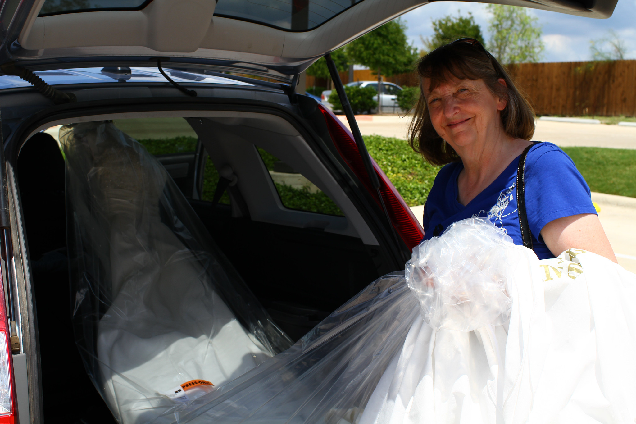 Eine ältere Frau holt ein Brautkleid aus dem Kofferraum ihres Autos | Quelle: Flickr