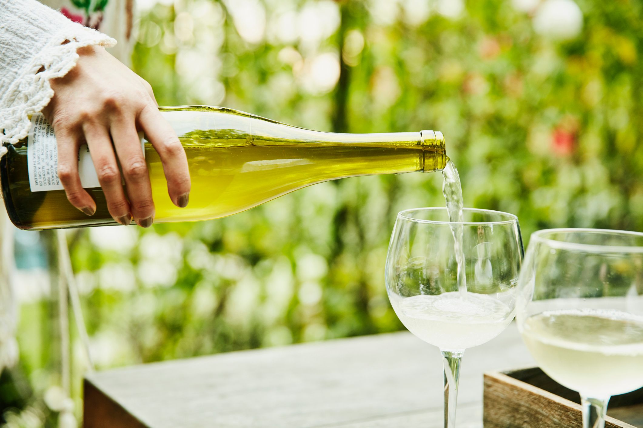 Woman pouring white wine into glasses in backyard. | Foto von: Stock-Fotografie via Getty Images