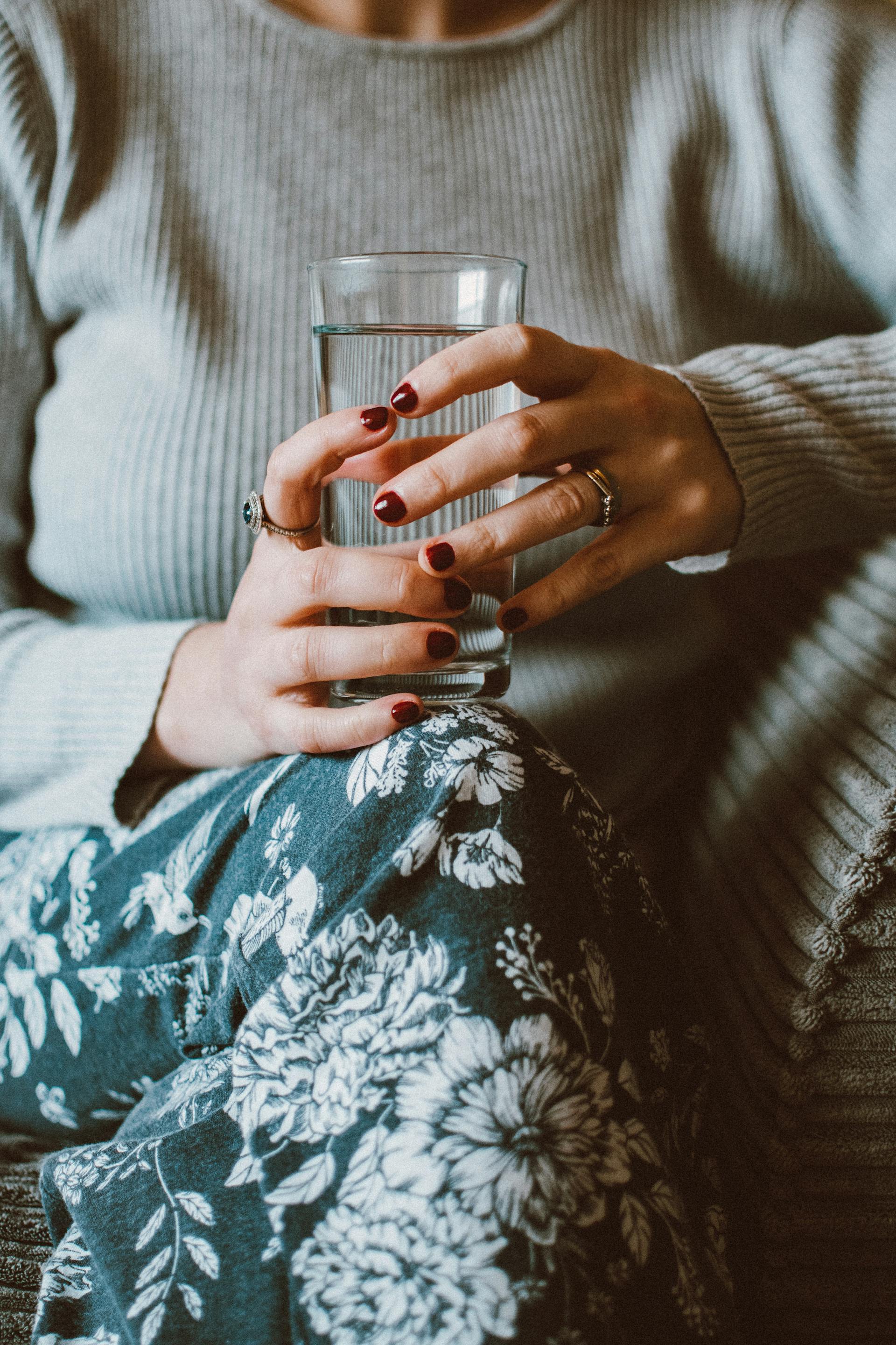 Eine Frau sitzt auf einem Sofa und hält ein Glas Wasser in der Hand | Quelle: Pexels