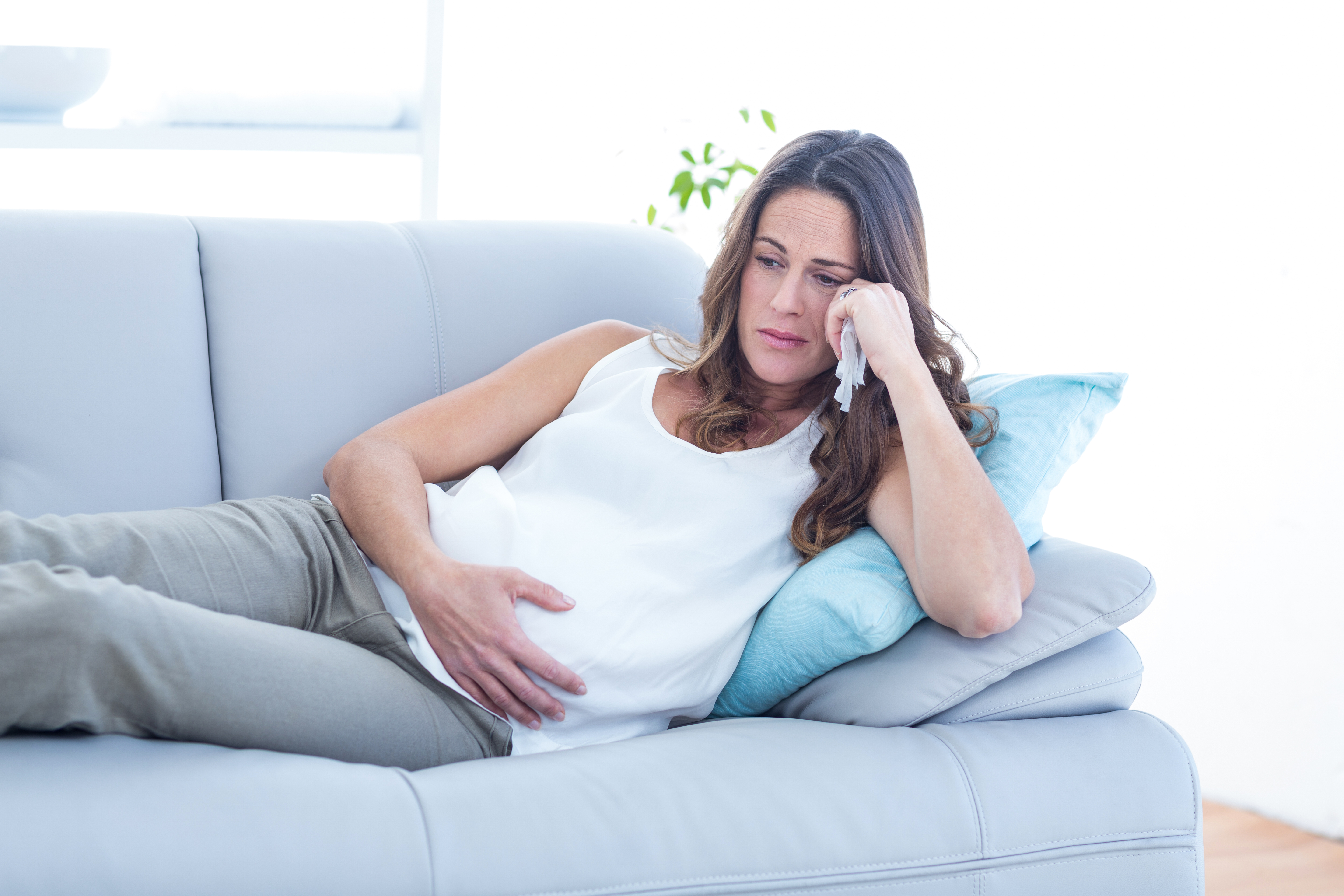 Eine schwangere Frau sitzt auf einer Couch und sieht traurig aus | Quelle: Shutterstock