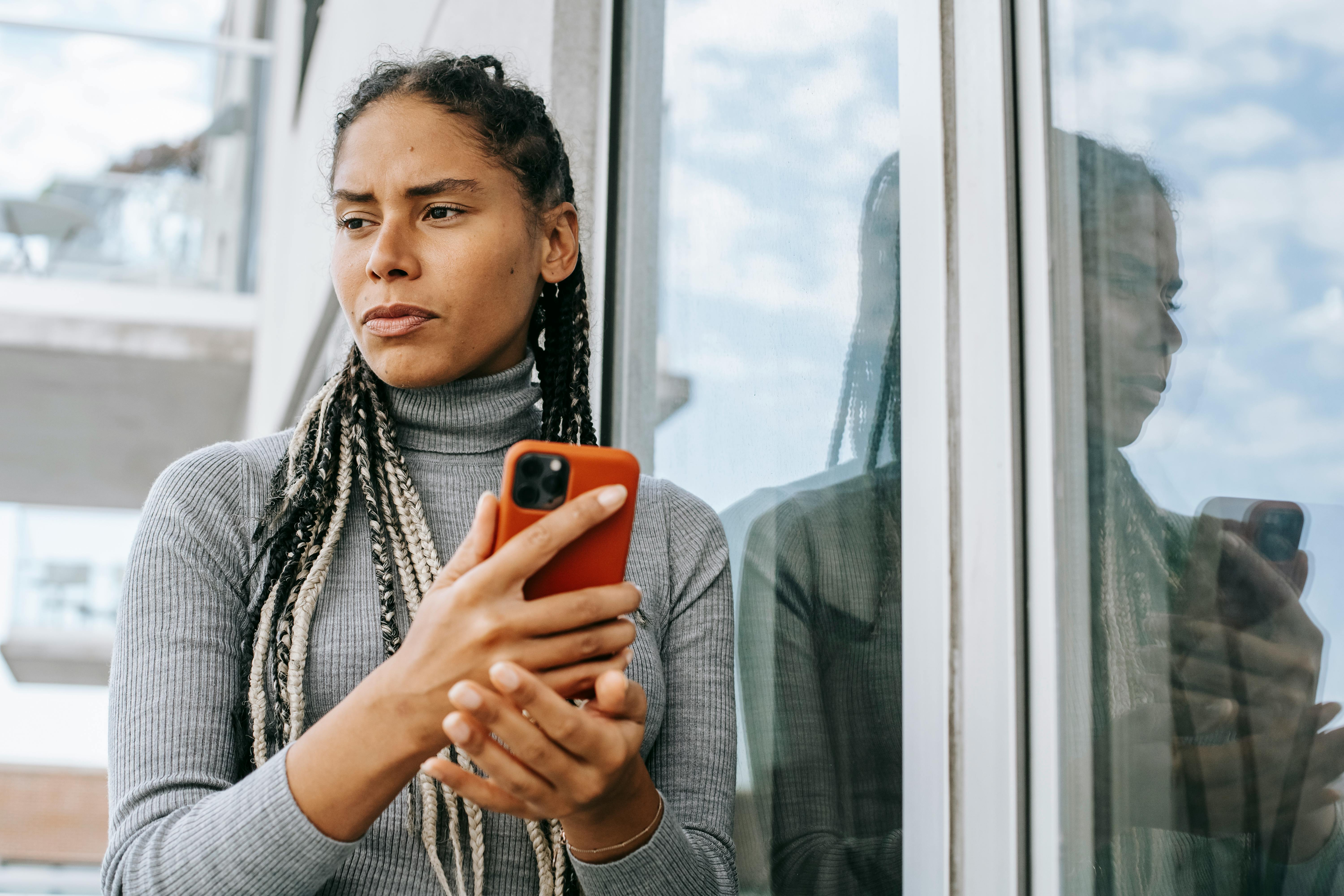 Eine Frau schaut zur Seite, während sie mit ihrem Handy in der Hand über etwas nachdenkt | Quelle: Pexels