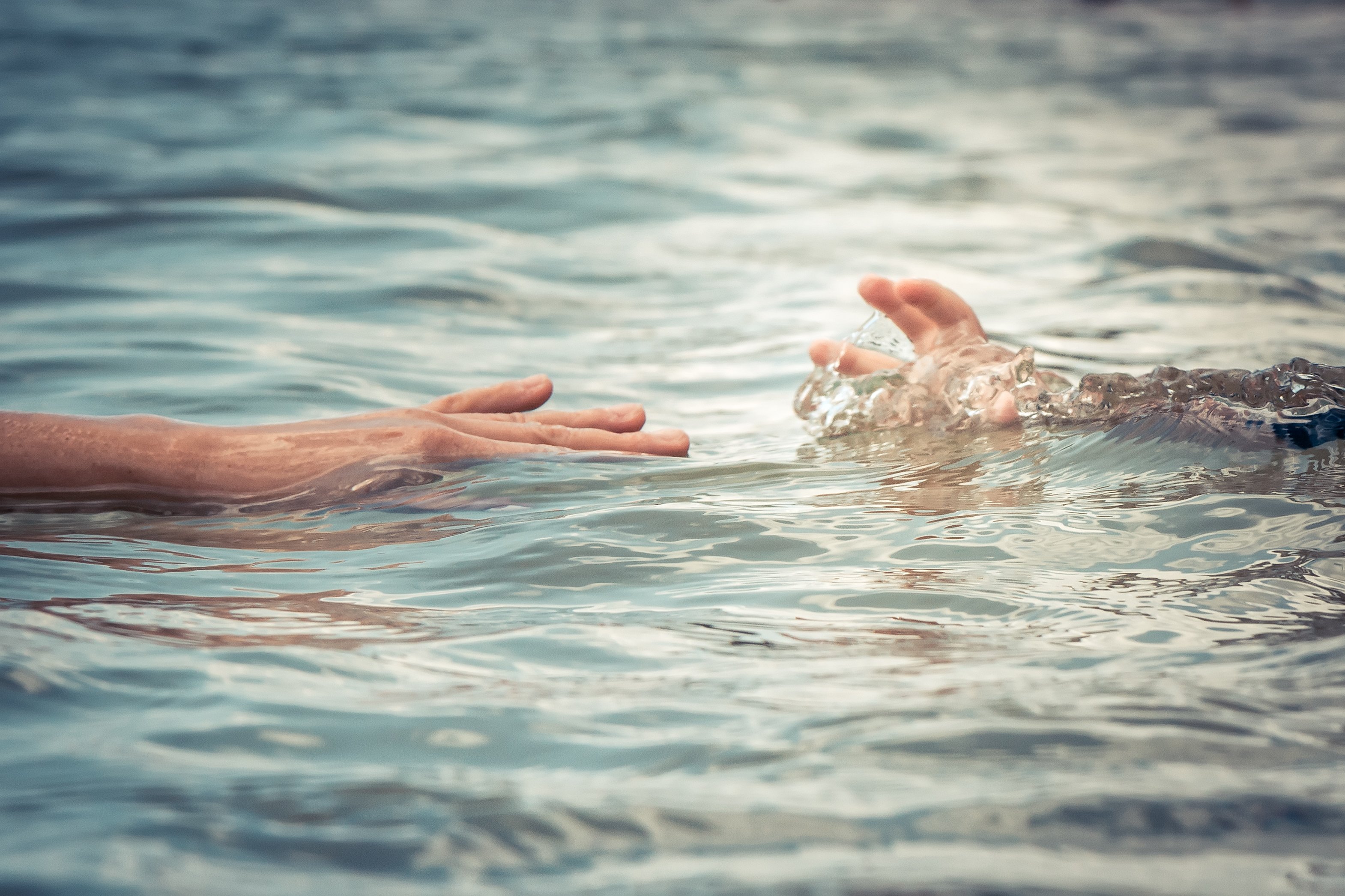 Eine helfende Hand eines Erwachsenen, die die Hand eines im Wasser ertrinkenden Kindes erreicht | Quelle: Getty Images