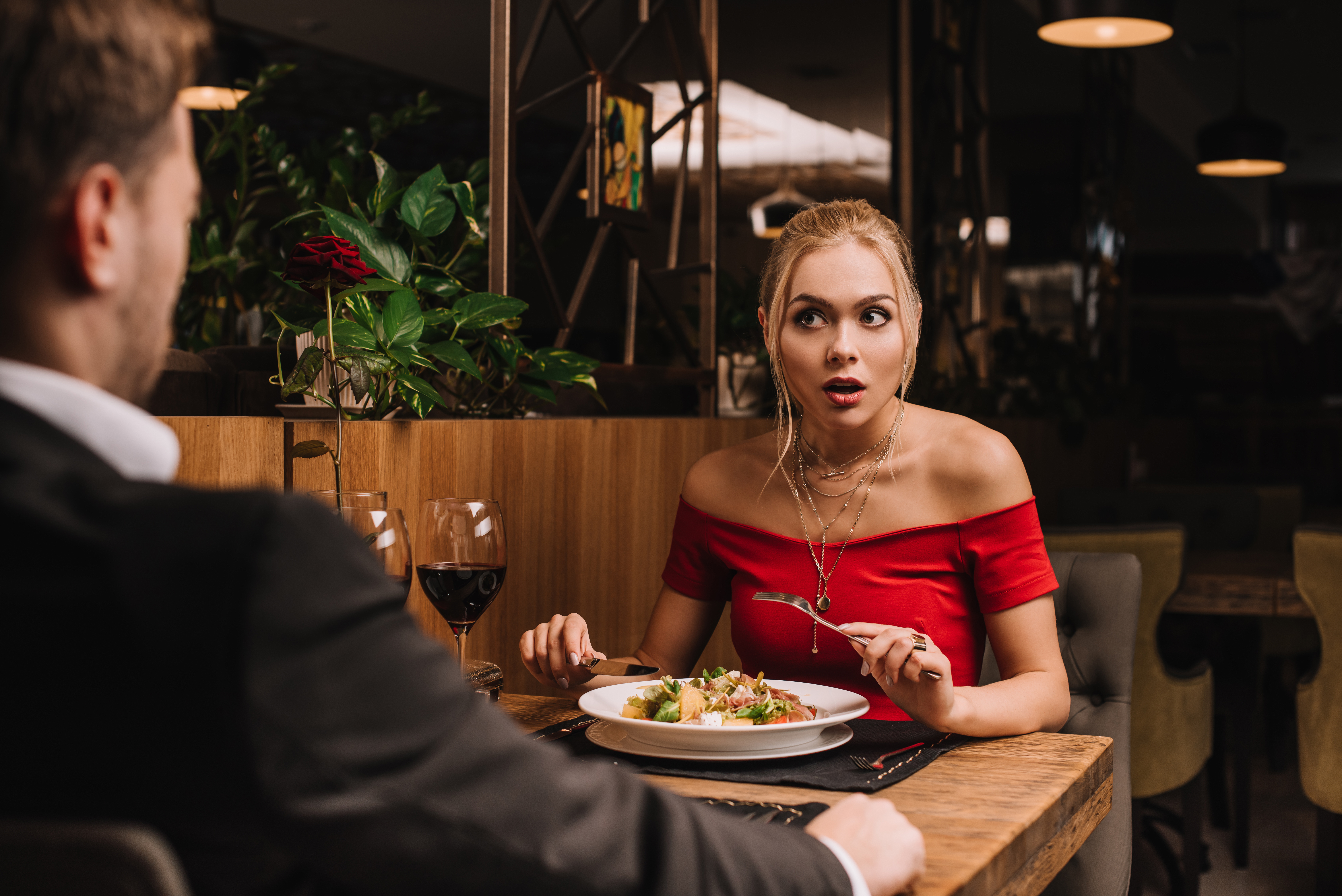 Eine junge Frau schaut den Mann beim Abendessen schockiert an | Quelle: Shutterstock