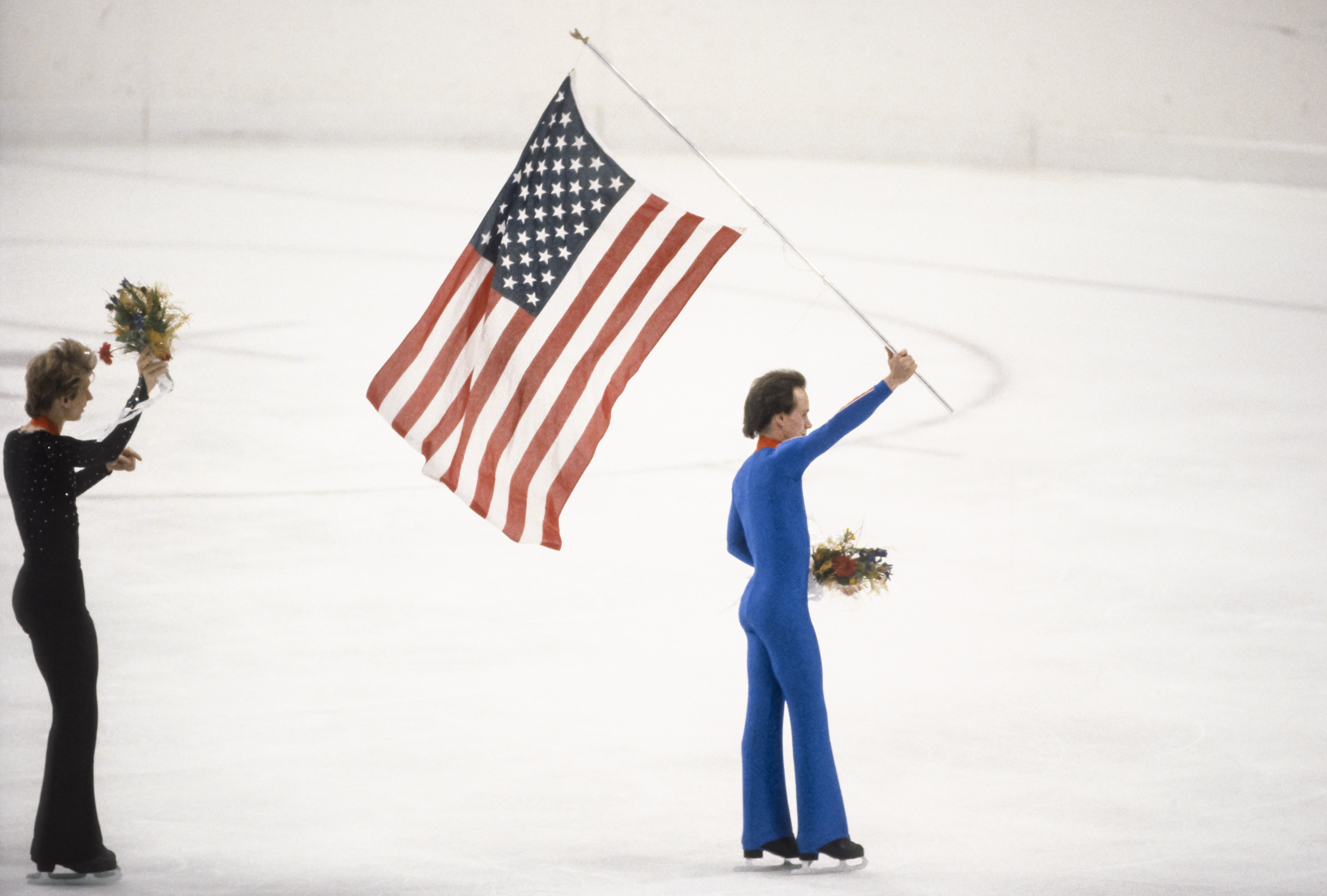 Scott Hamilton (USA) läuft mit der Flagge der USA nach der Medaillenzeremonie des Einzelwettbewerbs der Männer bei den Olympischen Winterspielen 1984 in Sarajevo, Jugoslawien am 16. Februar 1984, übers Eis | Quelle: Getty Images