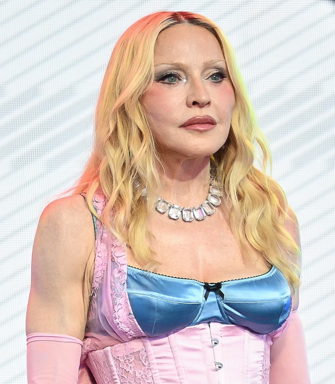 Madonna posiert in einem rosa-blauen Outfit im Korsett-Stil, mit langen blonden Haaren, rosa Handschuhen und einer großen, mit Edelsteinen besetzten Halskette. | Quelle: Chat GPT