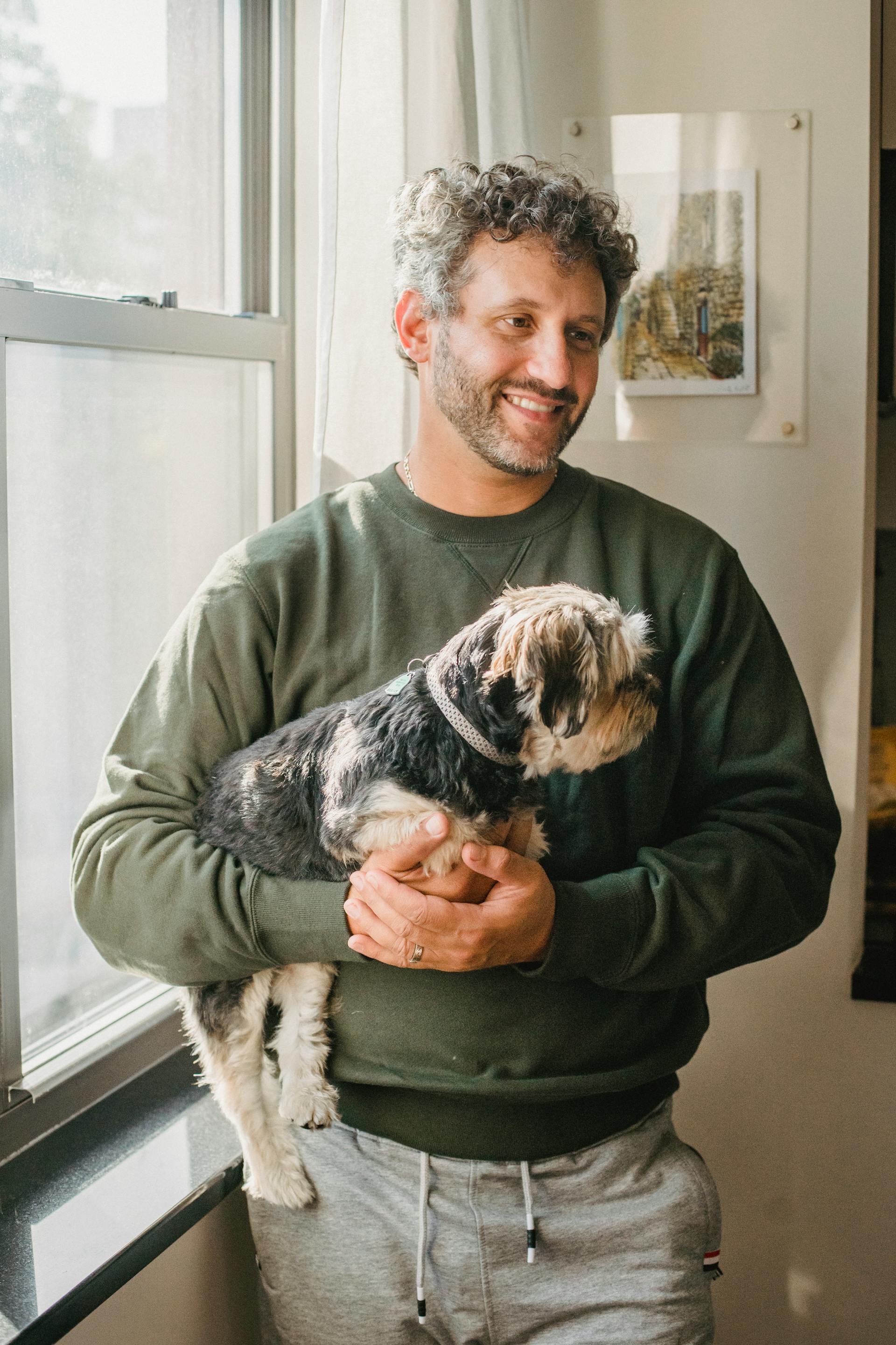 Ein Mann, der einen Hund hält, während er an einem Fenster steht | Quelle: Pexels