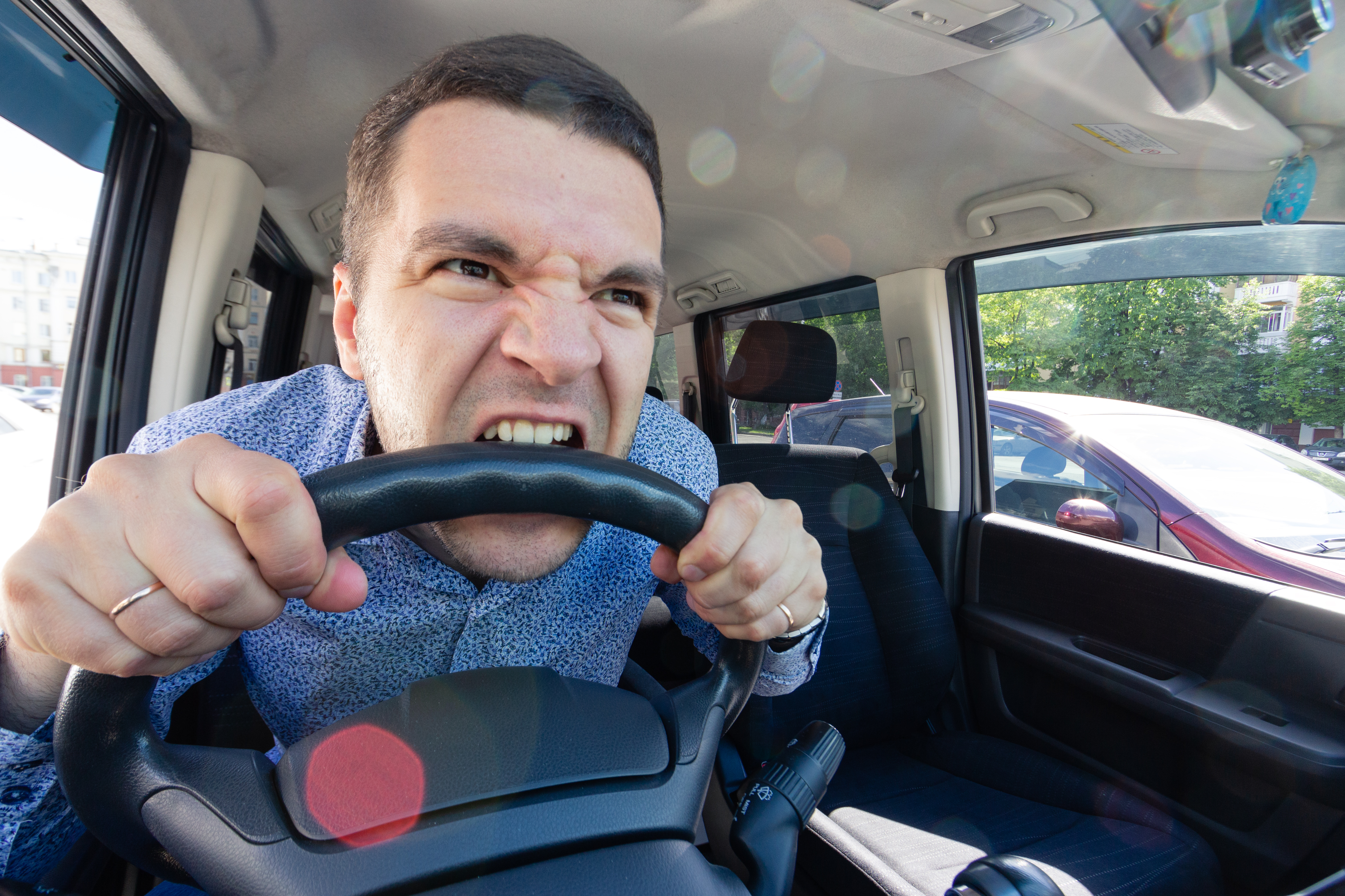 Ein wütender junger Mann beißt in das Lenkrad eines Autos | Quelle: Shutterstock
