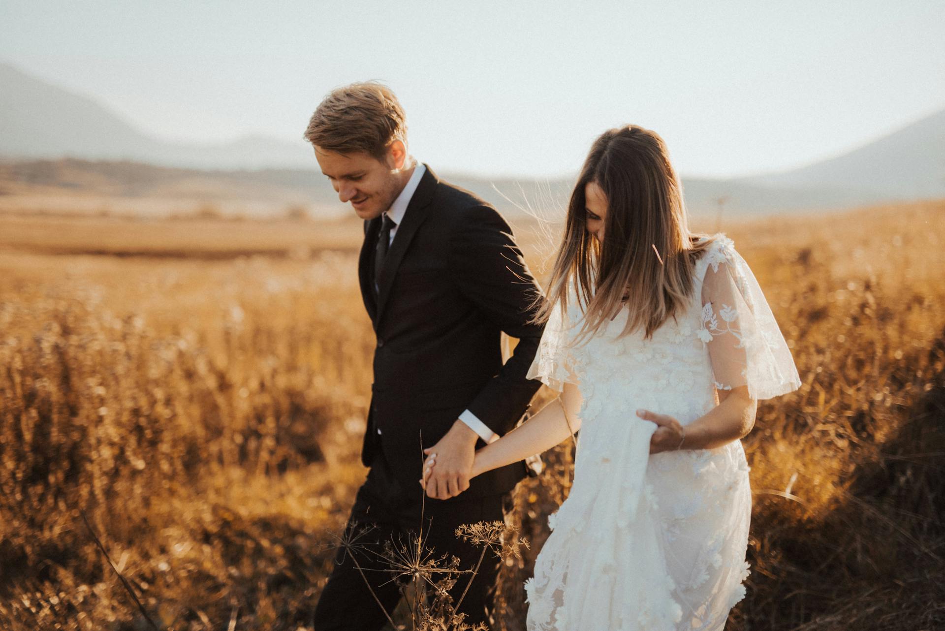 Eine Braut und ein Bräutigam halten sich auf einem Feld an den Händen | Quelle: Pexels