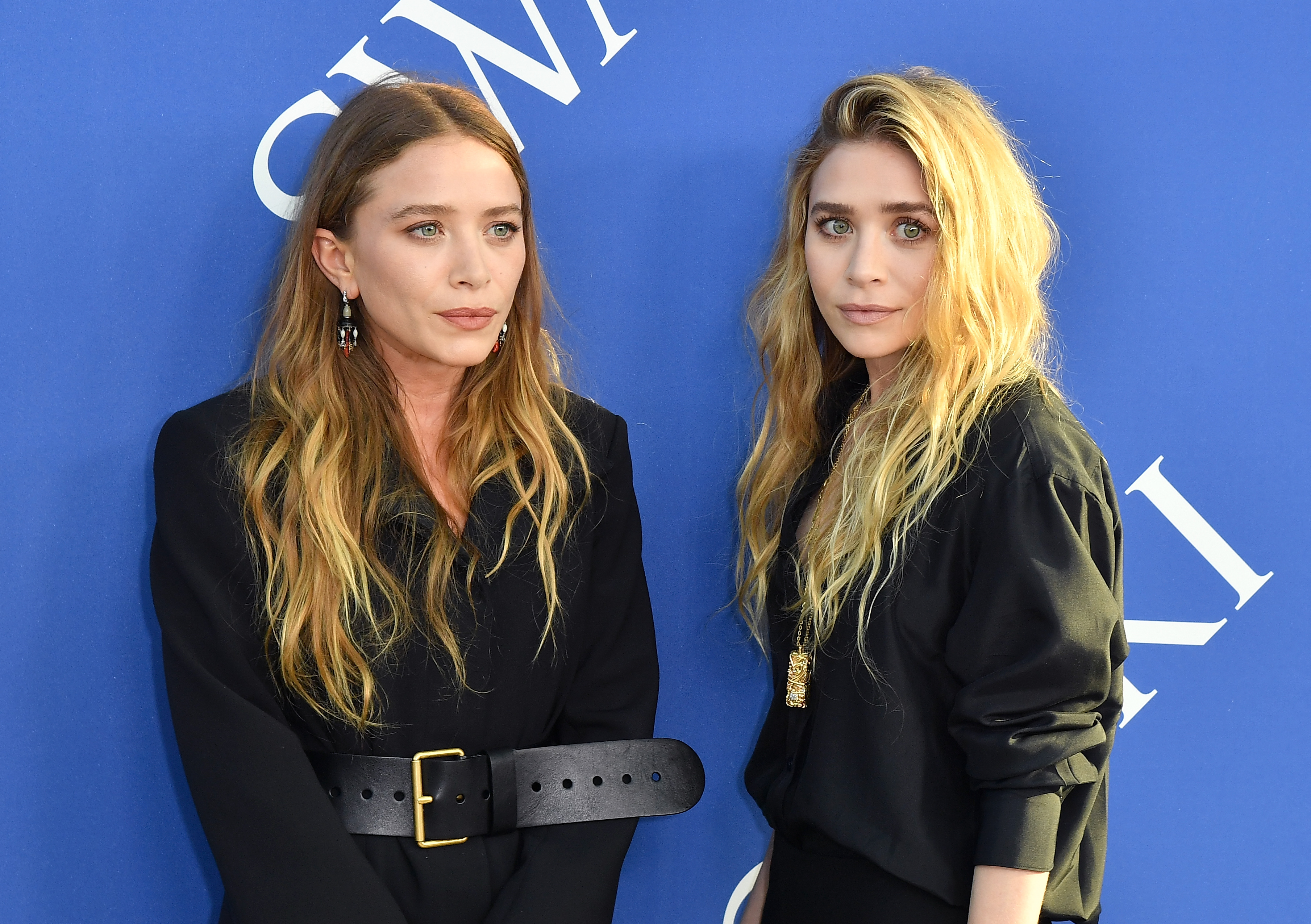 Markante Kinnlinien, ausgeprägte Wangenknochen, und durchdringende, direkte Blicke prägten das Erscheinungsbild der 31-jährigen Mary-Kate und Ashley Olsen bei den CFDA Fashion Awards am 4. Juni 2018, wo ihre ausdrucksstarken Gesichter von langen, zerzausten blonden Locken und minimalistischen schwarzen Outfits mit auffälligen Gürteln und Anhängerketten eingerahmt wurden.