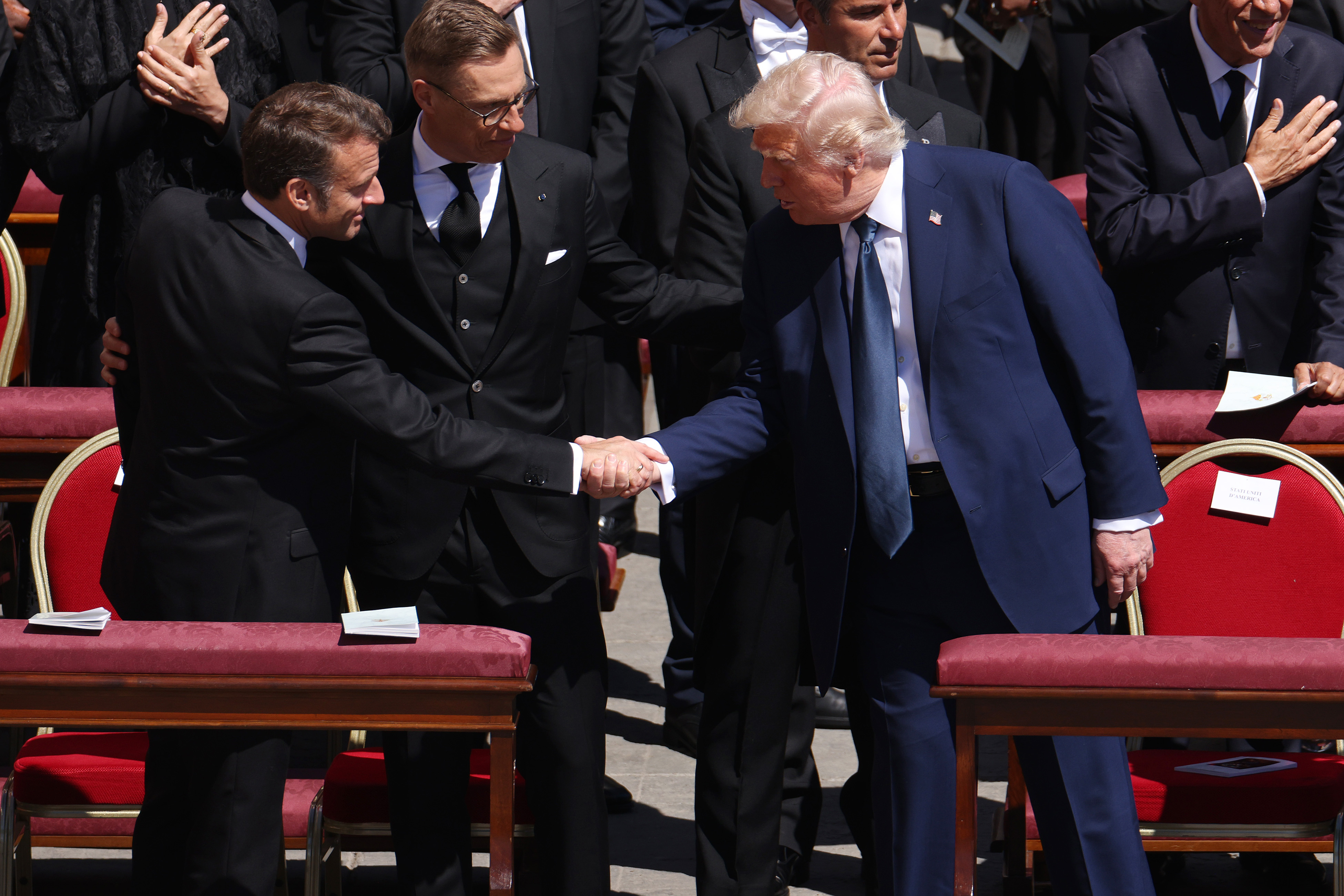 Emmanuel Macron und Donald Trump geben sich die Hand, während Alexander Stubb zwischen ihnen steht. | Quelle: Getty Images