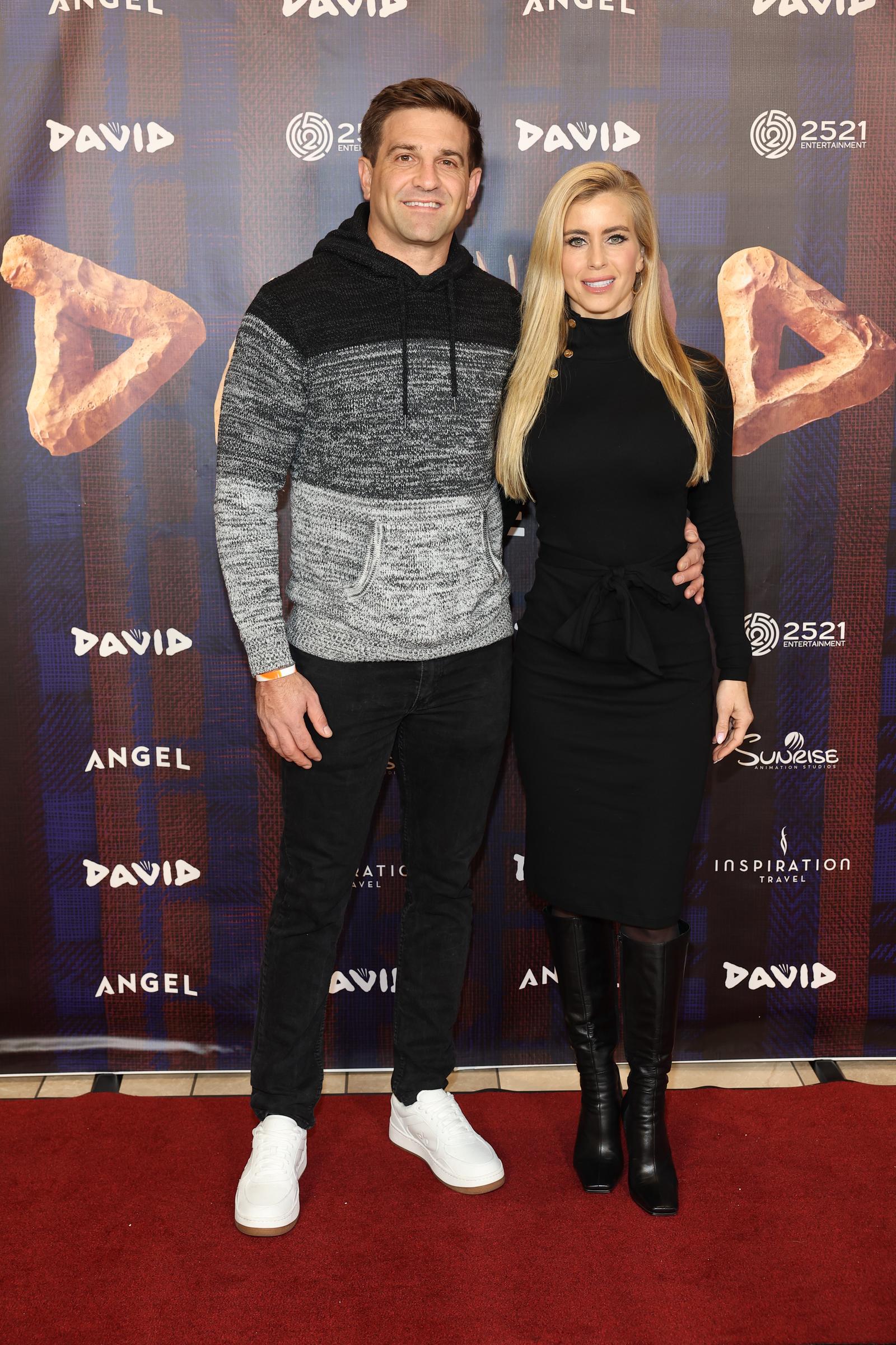 Tyler Zacharia und Katie Zacharia posieren in voller Länge auf dem roten Teppich bei der Premiere von „David“ im AMC DINE-IN Thoroughbred 20 am 14. Dezember 2025 in Franklin, Tennessee. Vor dem „Step-and-Repeat“-Hintergrund der Angel Studios präsentieren sie ihre Schuhe und ihre gesamte Silhouette: Tyler kombiniert schlichte weiße Low-Top-Sneaker mit seinem zweifarbigen Kapuzenpullover aus Strick und einer schwarzen Jeans, während Katie ihr schwarzes, knielanges Kleid mit Gürtel durch elegante schwarze kniehohe Lederstiefel abrundet. | Quelle: Getty Images