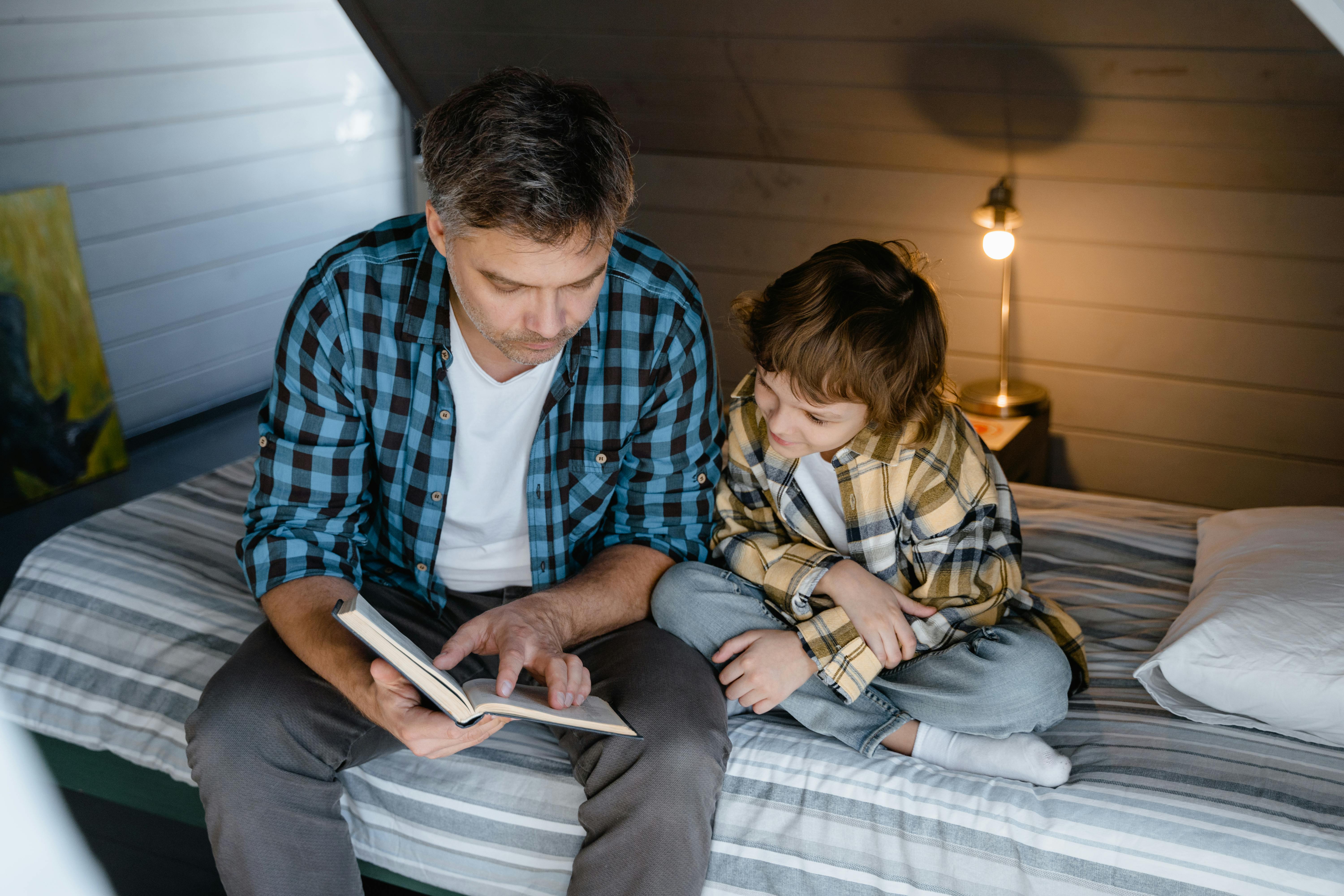 Ein Mann liest einem Jungen vor, der zusammen auf einem Bett sitzt | Quelle: Pexels