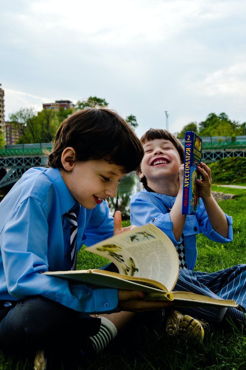 Zwei Jungen, die lachend im Gras sitzen und Bücher lesen | Quelle: Pexels