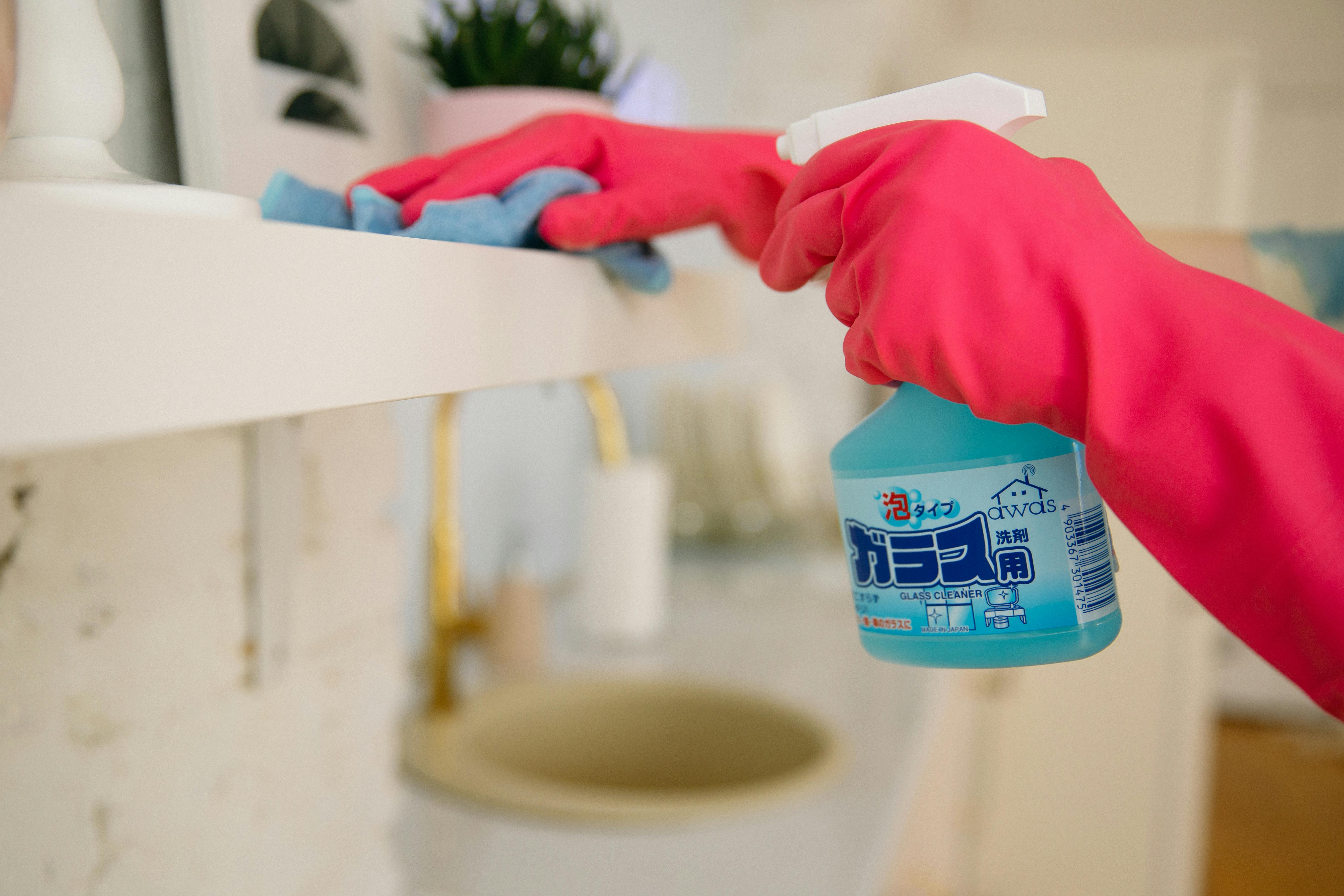 Eine Person mit Handschuhen hält eine Sprühflasche mit Glasreiniger | Quelle: Pexels