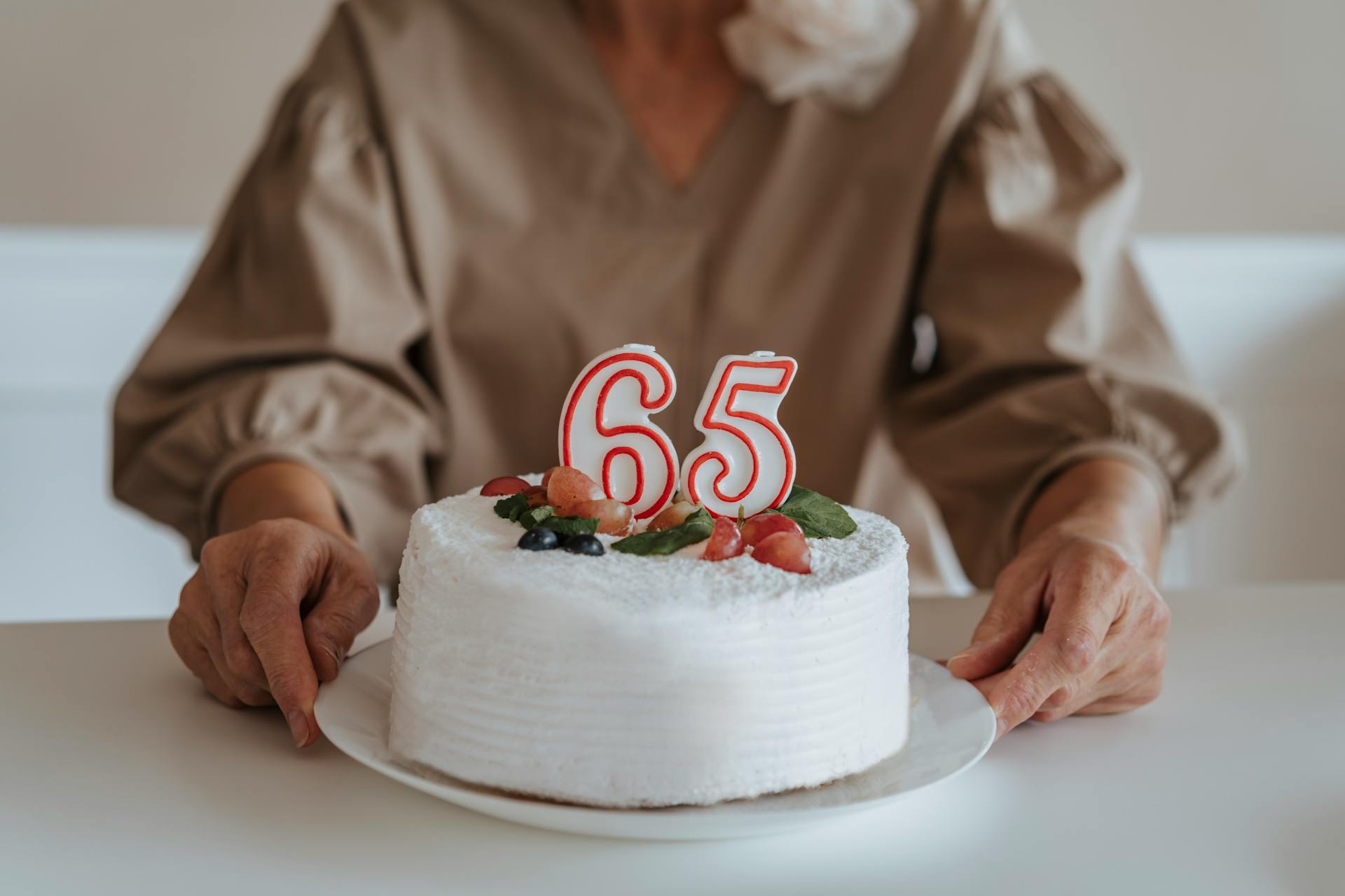 Beschnittene Aufnahme einer älteren Frau, die ihren 65. Geburtstagskuchen hält | Quelle: Pexels
