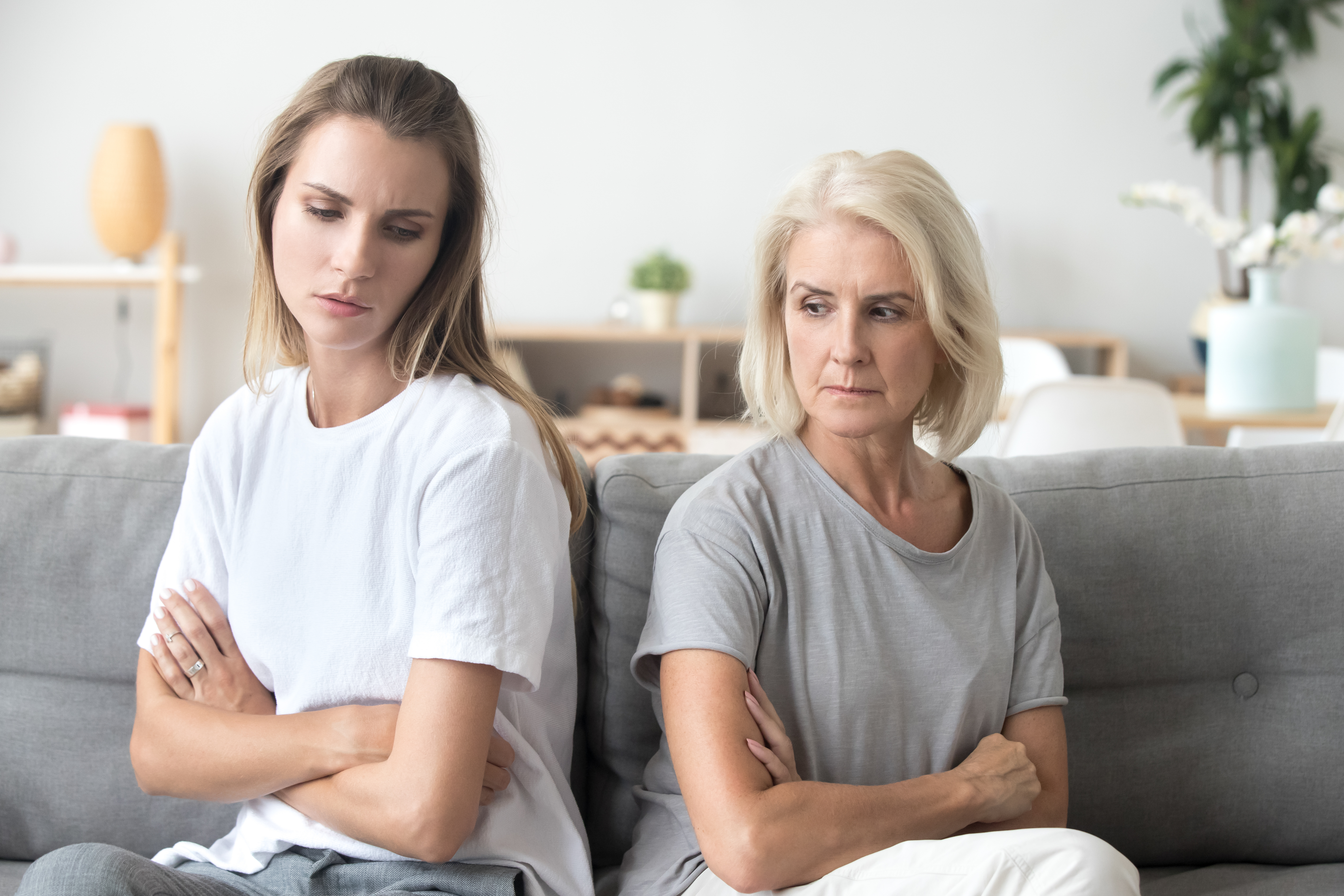 Eine jüngere Frau misstraut einer älteren Frau, beide sitzen mit dem Rücken zueinander | Quelle: Shutterstock