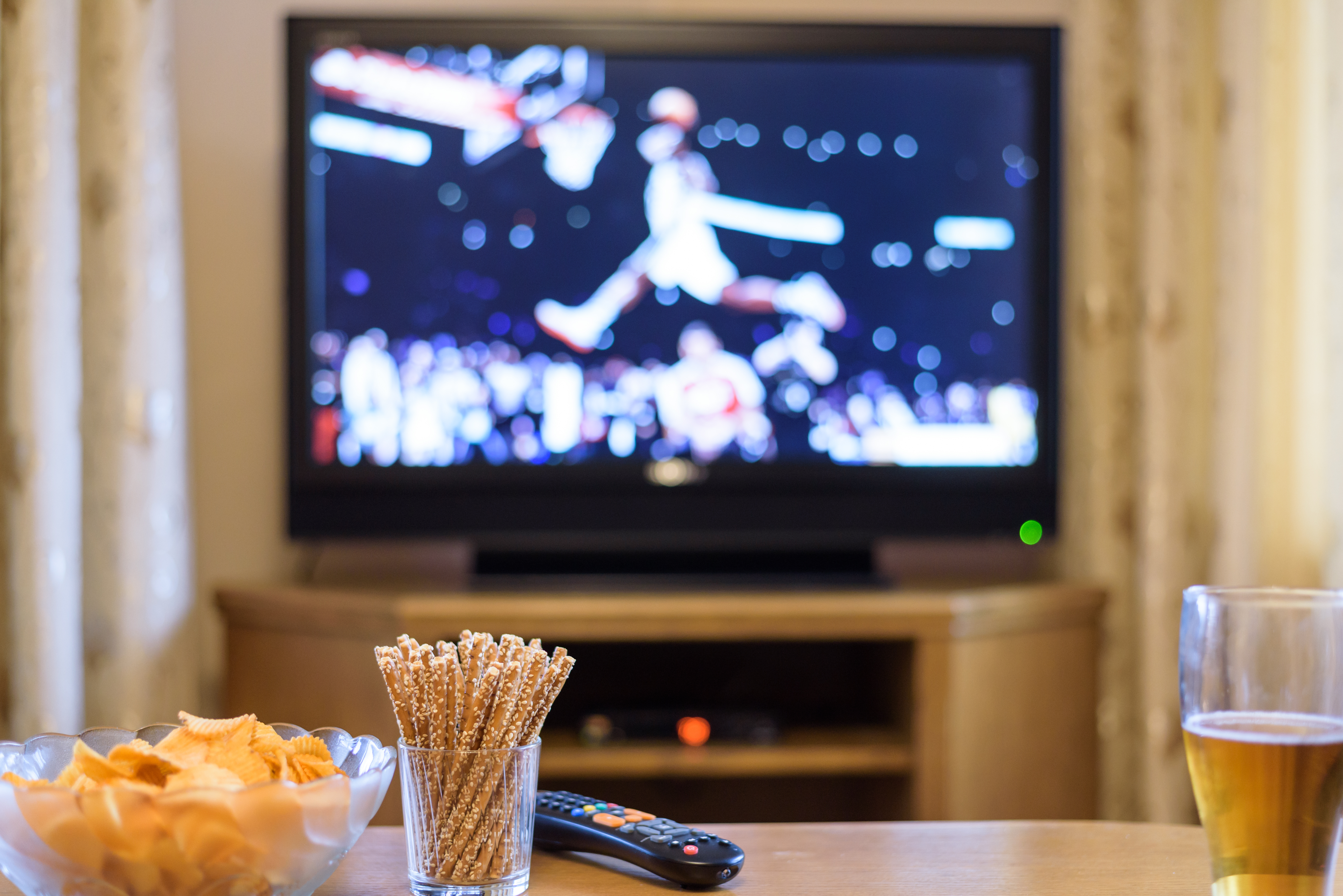 Snacks auf einem Couchtisch vor der Kulisse eines Basketballspiels im Fernsehen | Quelle: Shutterstock