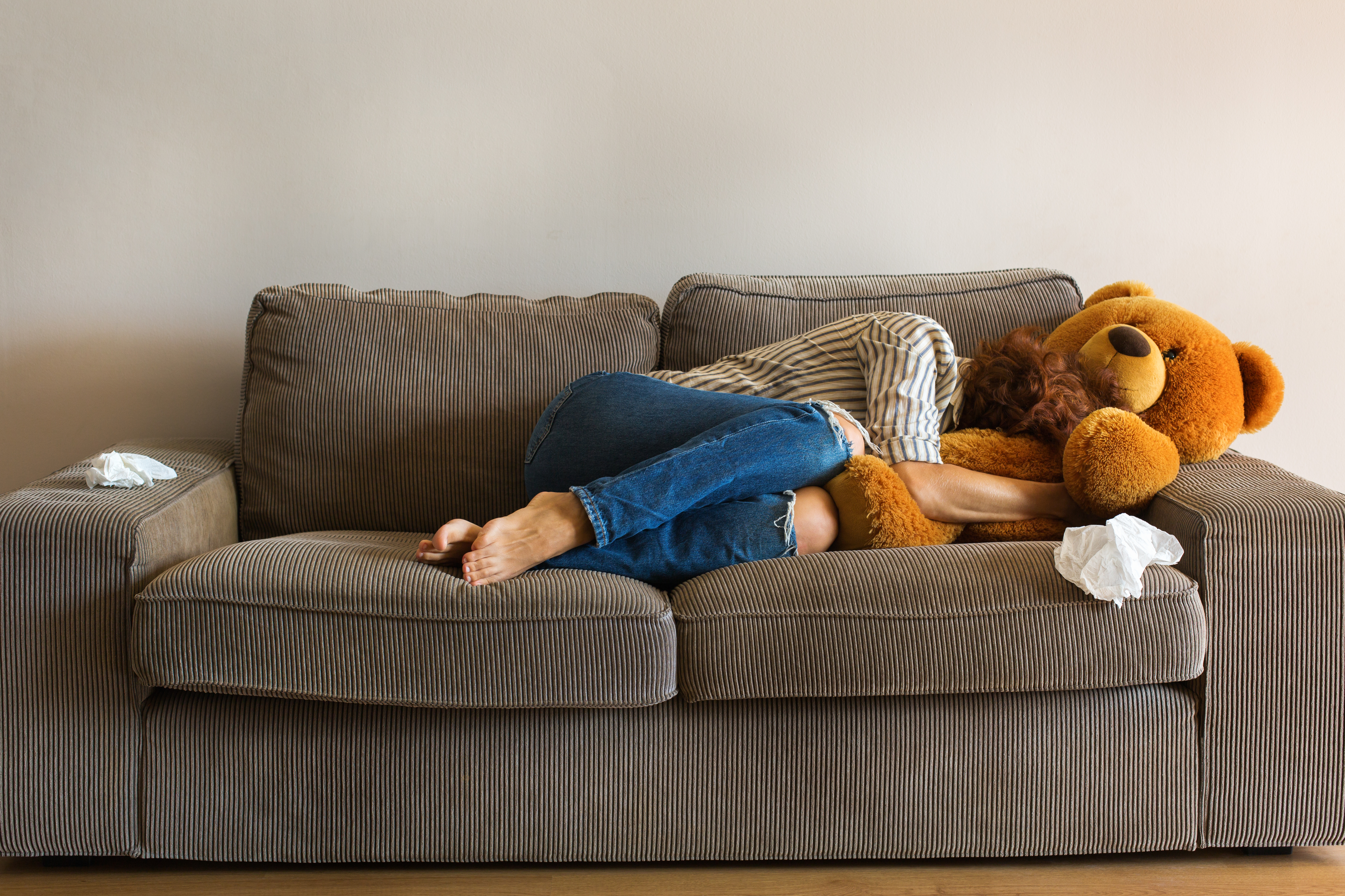 Eine deprimierte junge Frau liegt auf der Couch und weint, während sie einen Teddybär umarmt | Quelle: Shutterstock