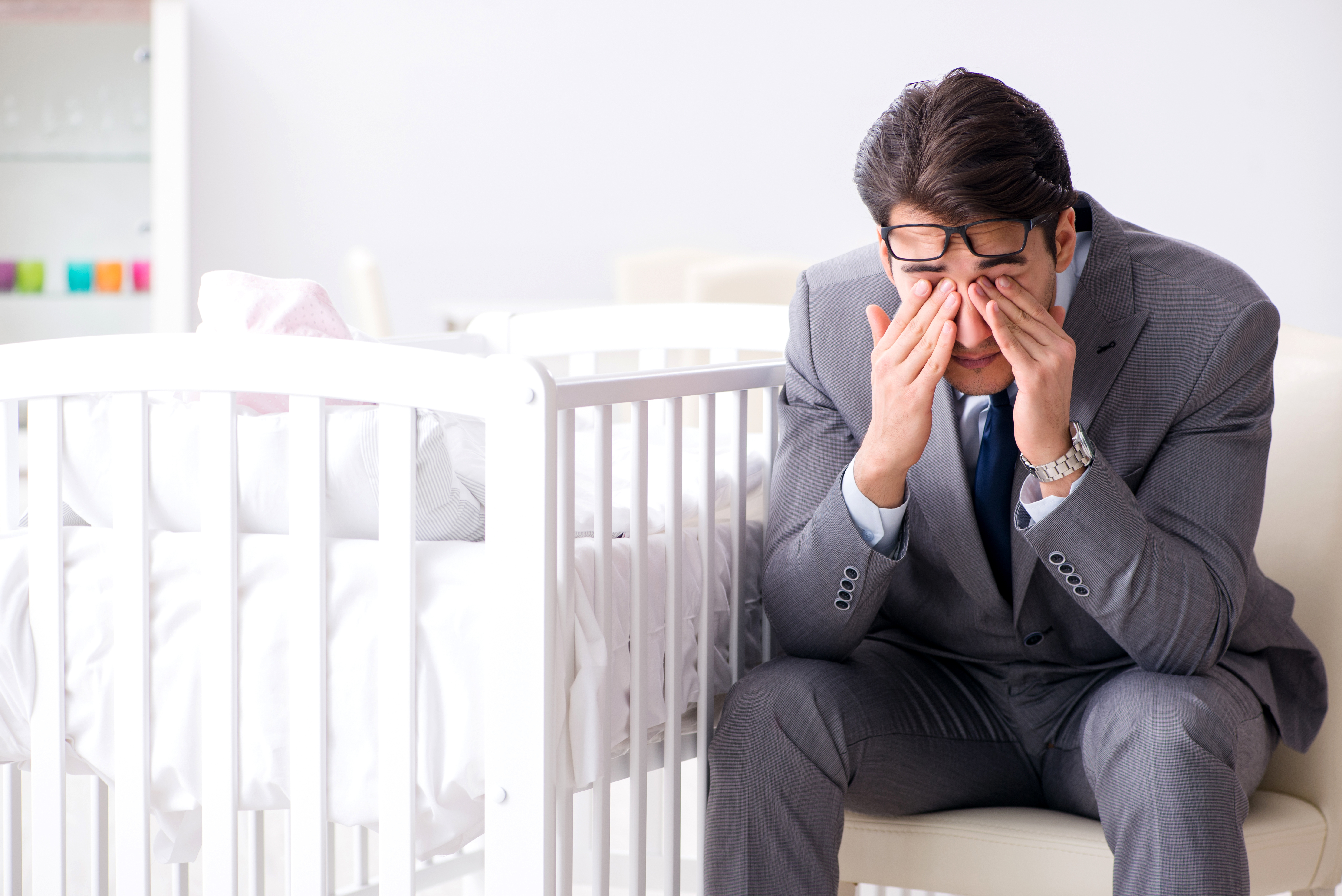 Ein emotional beeinträchtigter Mann sitzt neben einem leeren Kinderbett. | Quelle: Shutterstock