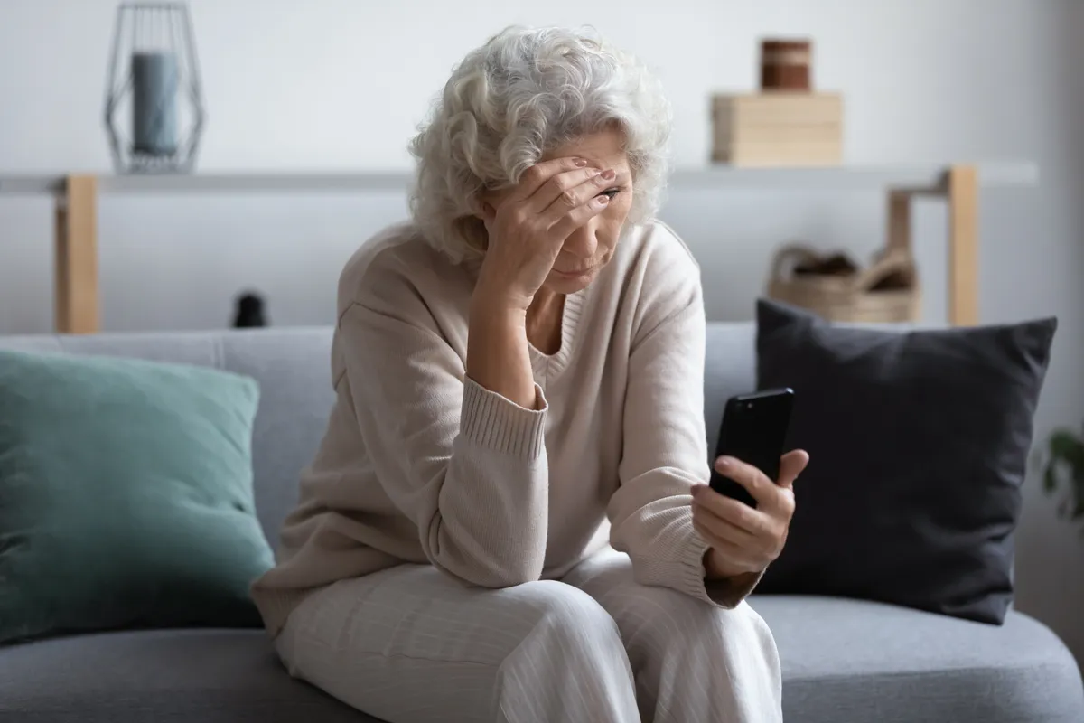 Eine unglückliche ältere Frau, die auf ihr Handy-Display schaut | Quelle: Shutterstock